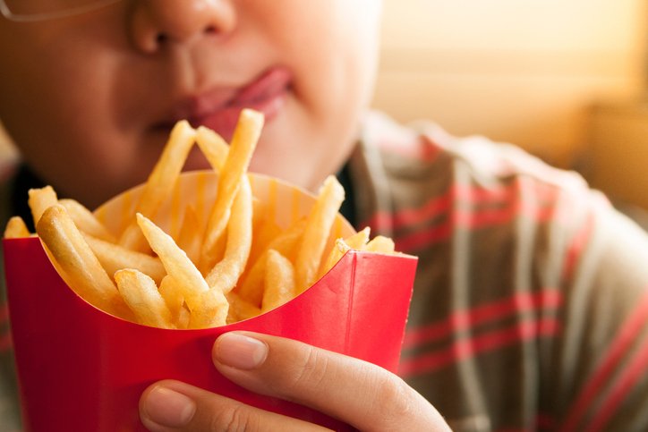 Geschnittenes Bild des verführten Jungen, der Pommes Frites-Paket hält | Quelle: Getty Images