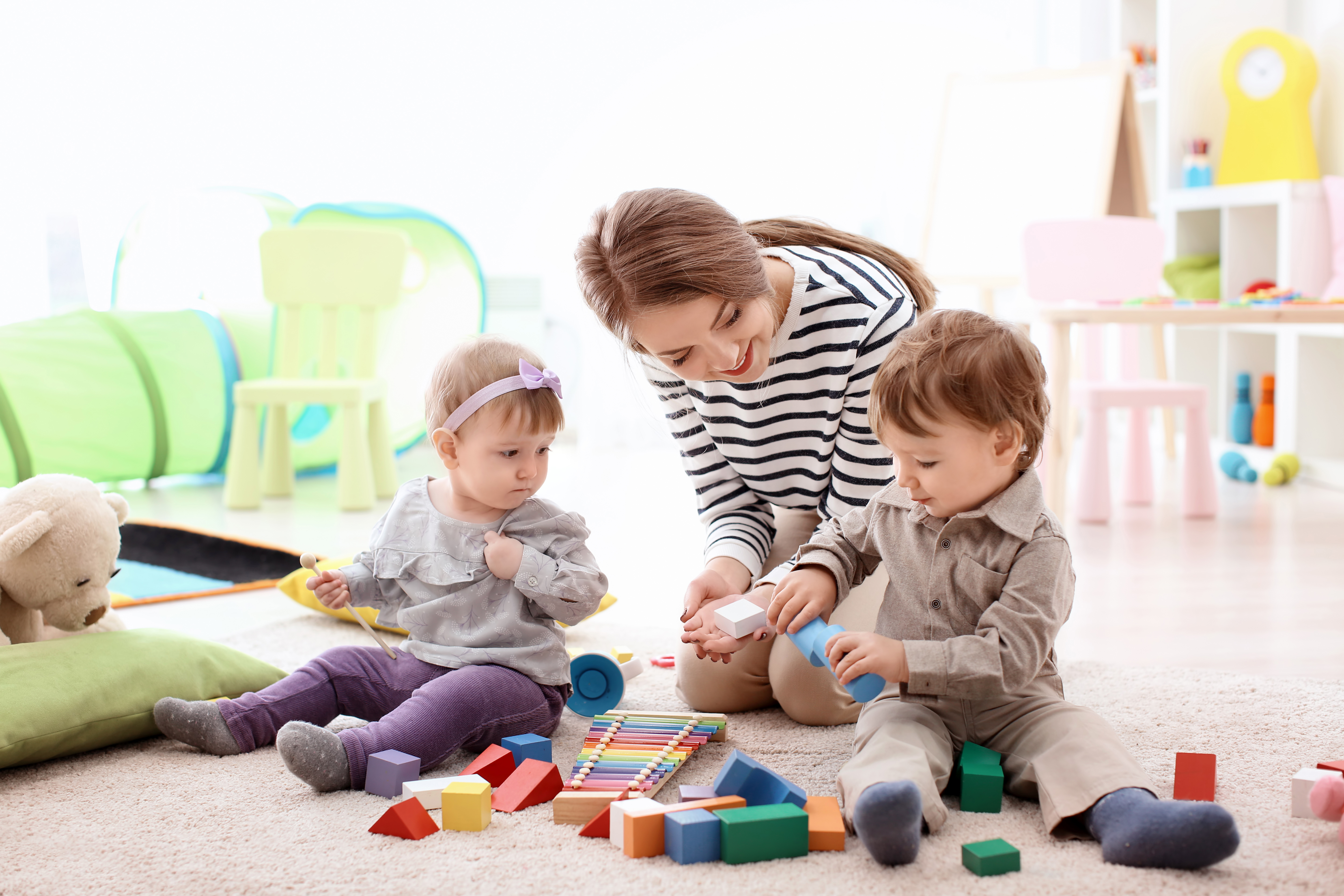 A young woman assisting two toddlers during playtime | Source: Shutterstock