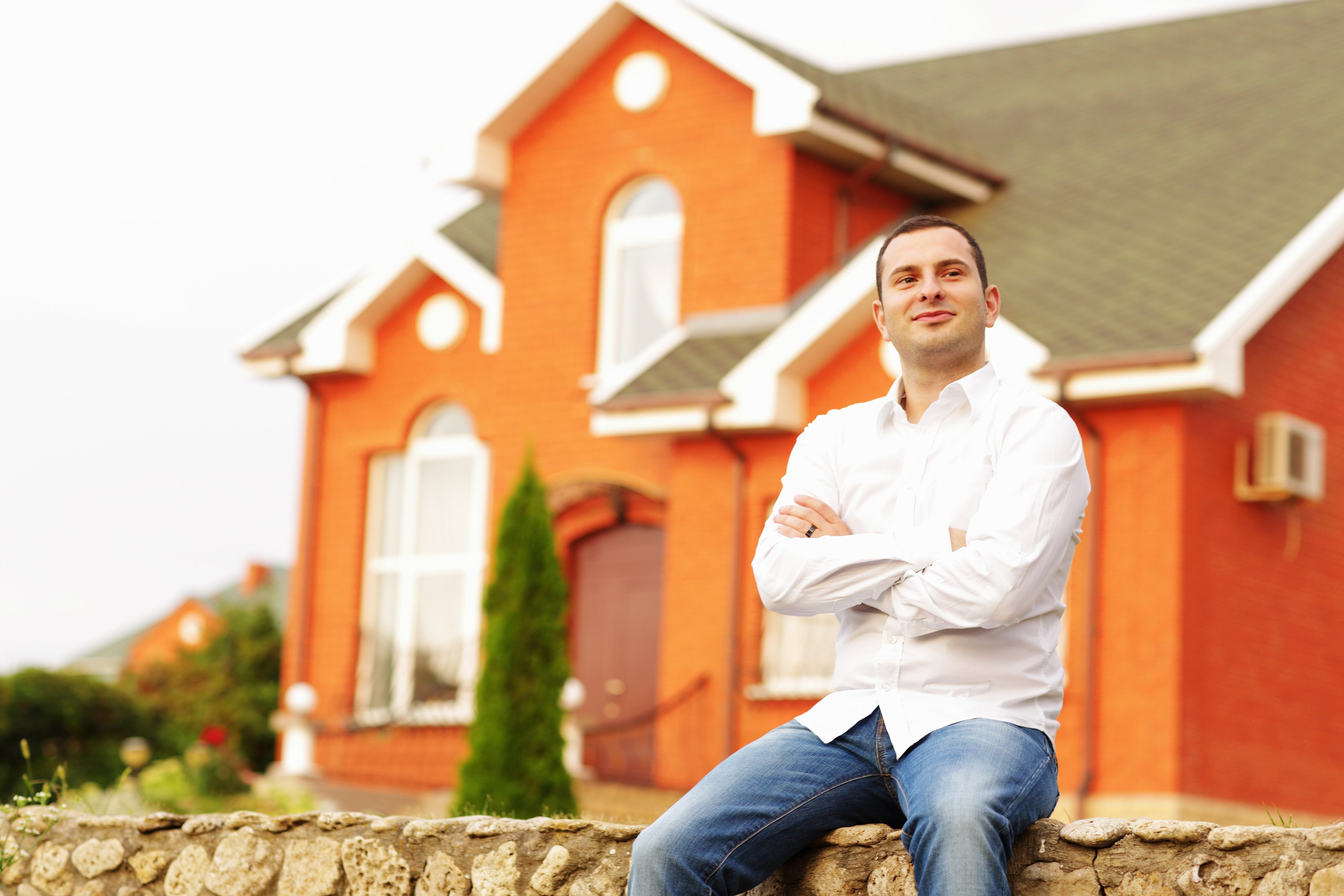 Happy man sitting in front of an orange-bricked house.|Source: Shutterstock