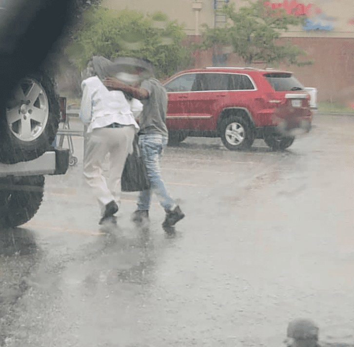 A young boy helping an elderly lady to her car in the rain. │Source: facebook.com/ipdinfo