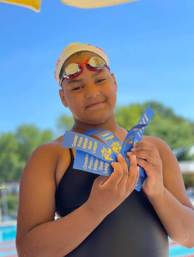 Carys Fairfax holds swim ribbons at a pool during a youth competition | Source: Facebook/justin.fairfax.2025