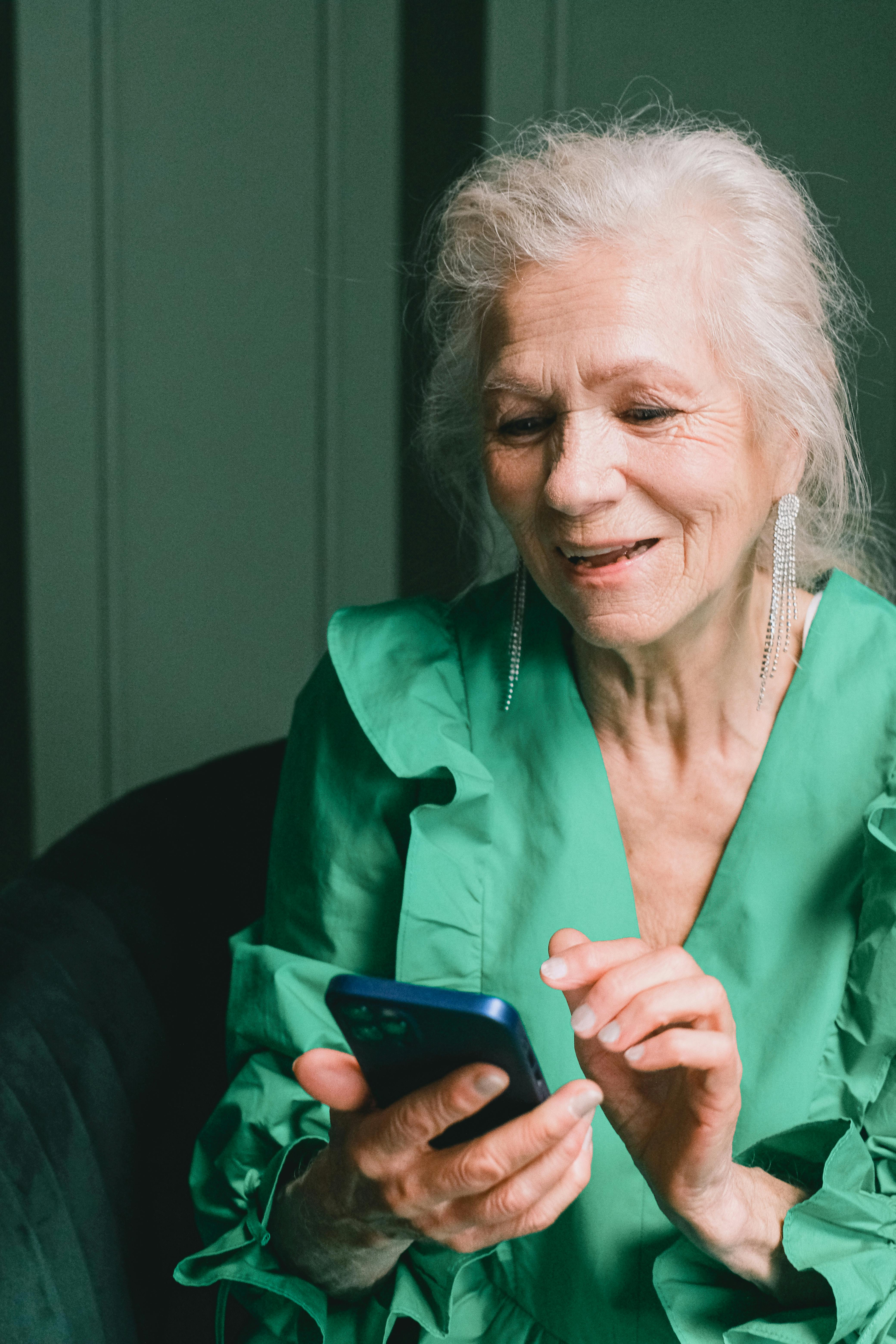 An older woman smiling while using a phone | Source: Pexels