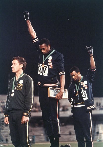 Gold medalist Tommie Smith (C) and bronze medalist John Carlos (R) of the United States raise their fists on the podium at the medal ceremony for the Athletics Men's 200m during the Mexico City Olympic Games at the Estadio Olimpico Universitario on October 14, 1968 in Mexico City, Mexico | Source: Getty Images