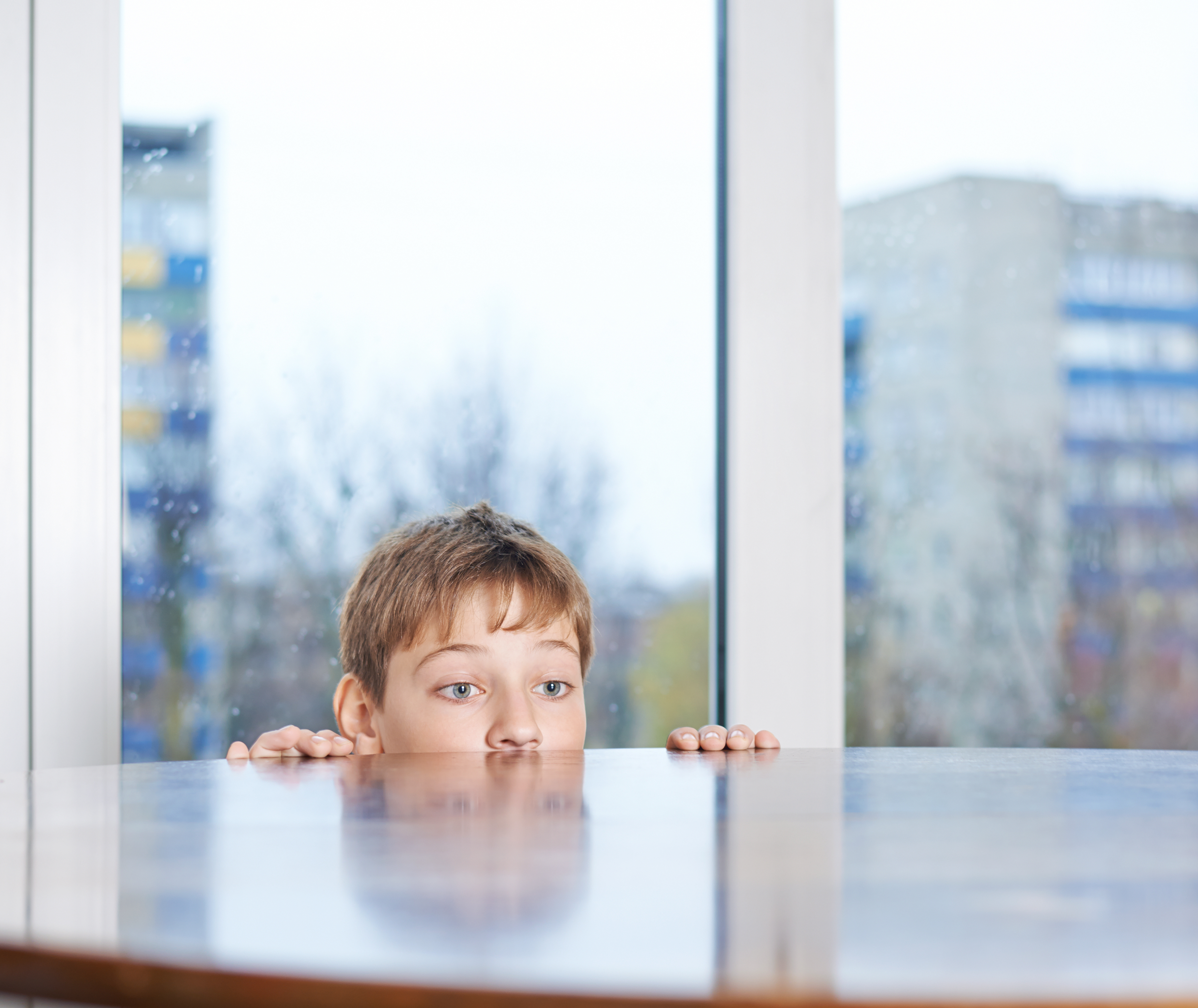 A young boy peeking from behind a wooden table | Source: Shutterstock