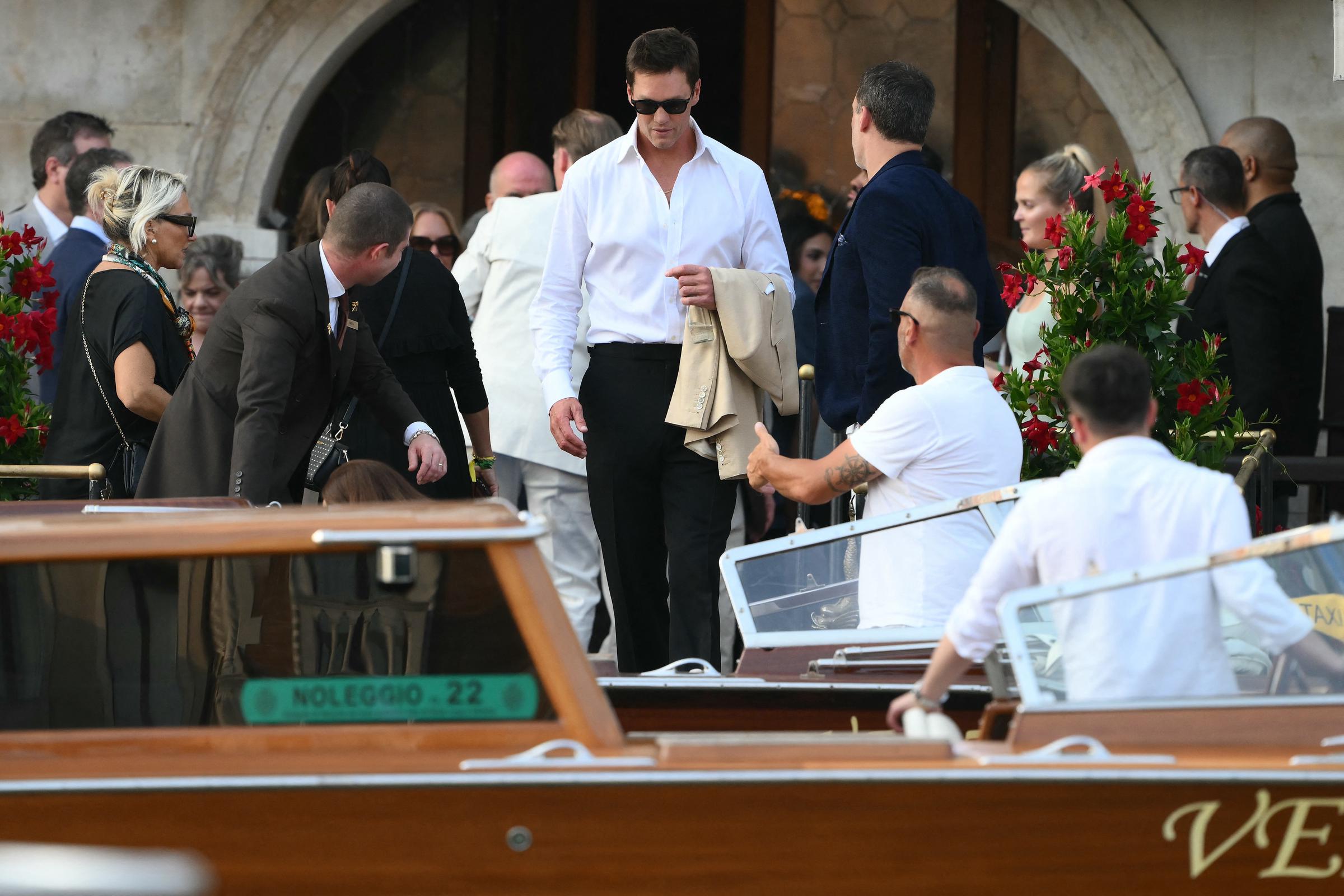 US football player Tom Brady gets on a taxi boat as he joins the many celebrities who attend the Amazon wedding in Venice. He steps out in a white shirt and black trousers while his cream-coloured jacket hangs on his arm. He pairs the classy yet simple outfit with sunglasses.