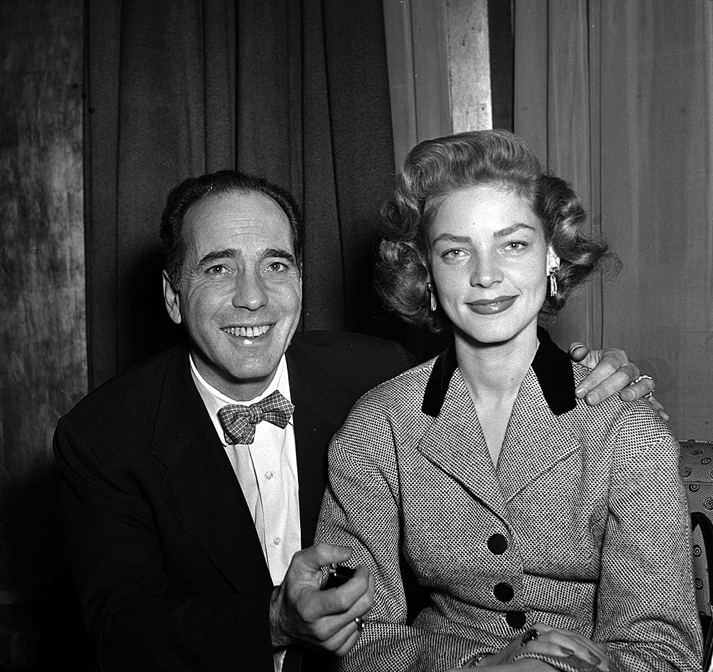 Humphrey Bogart lächelt mit seiner Schauspielerin Frau Lauren Bacall bei einem Presseempfang im Claridges in London, 1951. | Quelle: Getty Images
