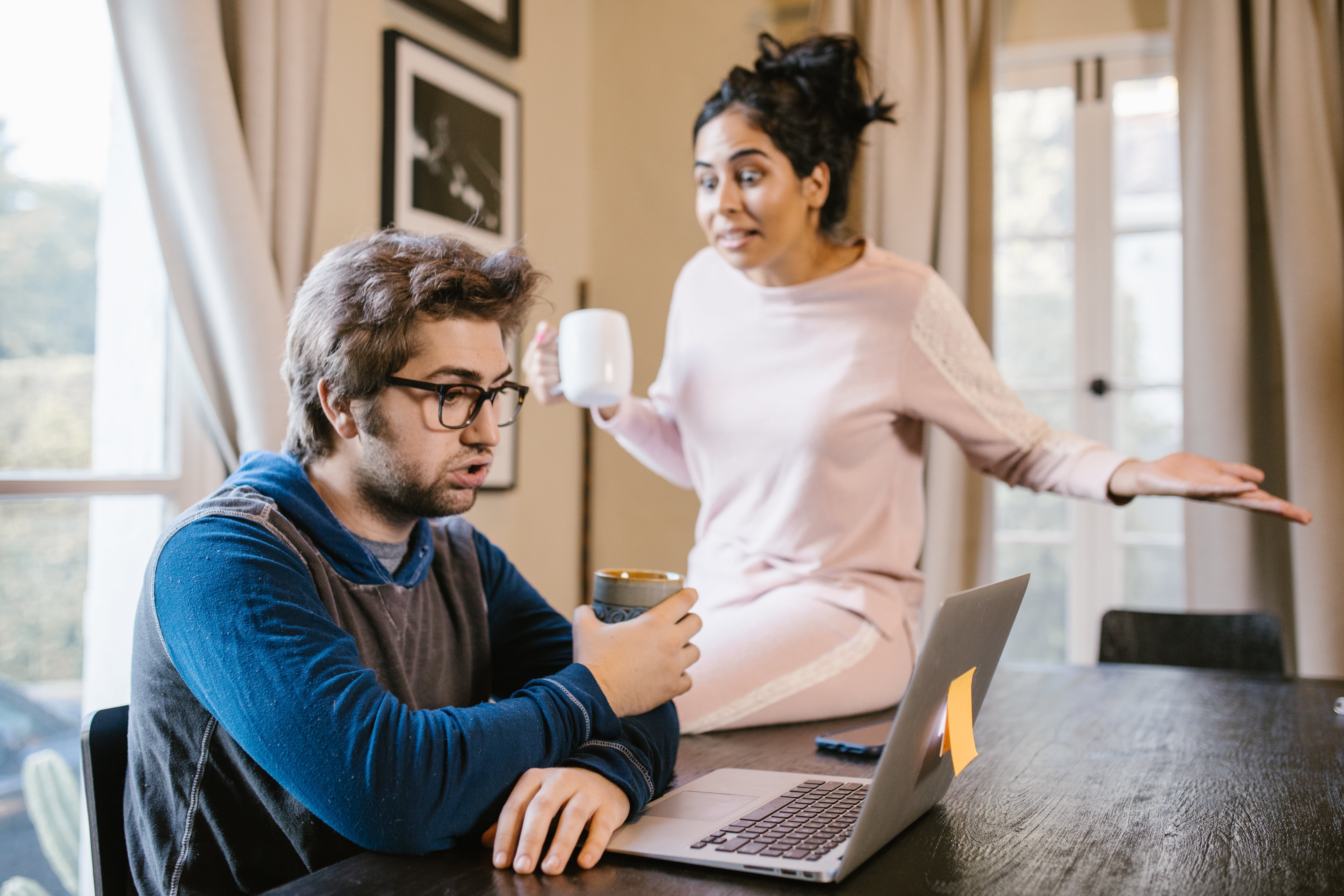 A couple holding mugs while one is seated in front of a computer and one is standing during an argument | Source: Pexels