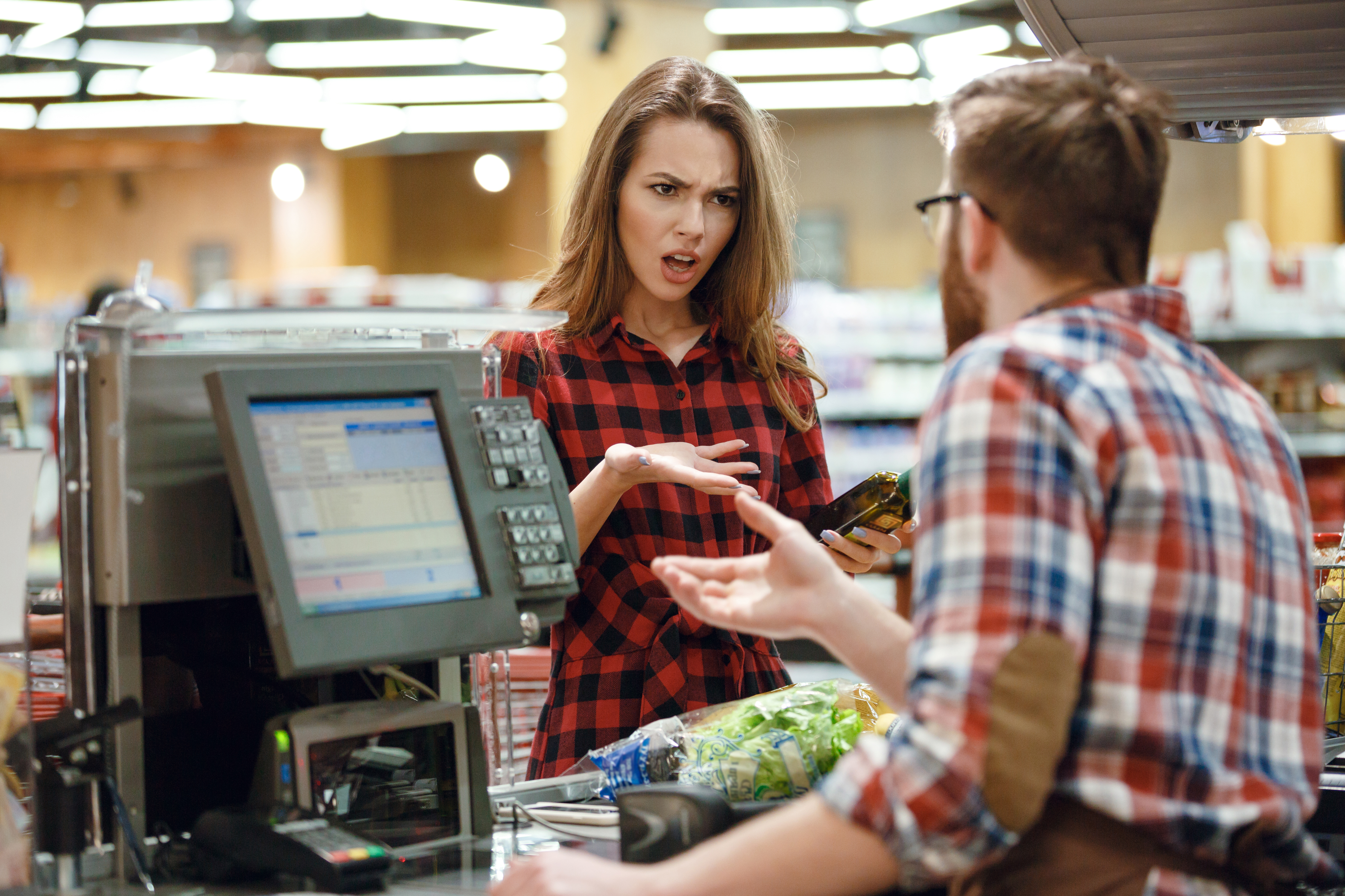 An angry female cashier attending to a male customer | Source: Shutterstock