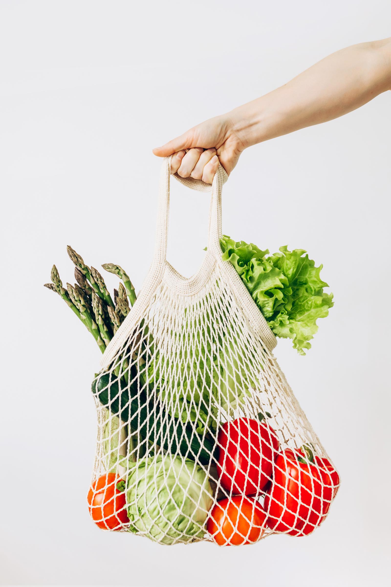 A female hand holds eco friendly mesh grocery shopping bag with mixed vegetables | Source: Getty Images