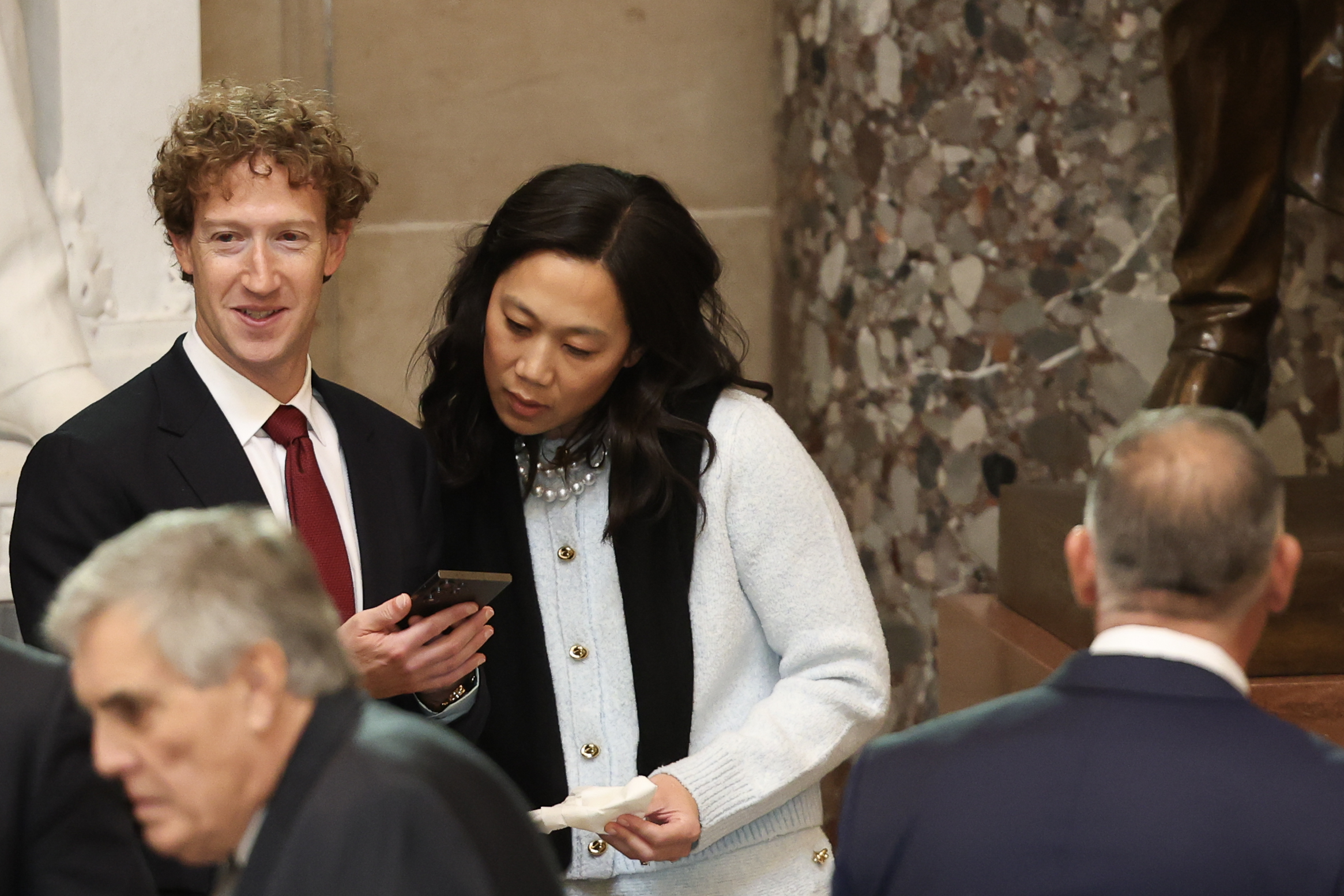 Priscilla Chan looking at Mark Zuckerberg's phone as they stand next to each other during Donald Trump's inauguration. | Source: Getty Images