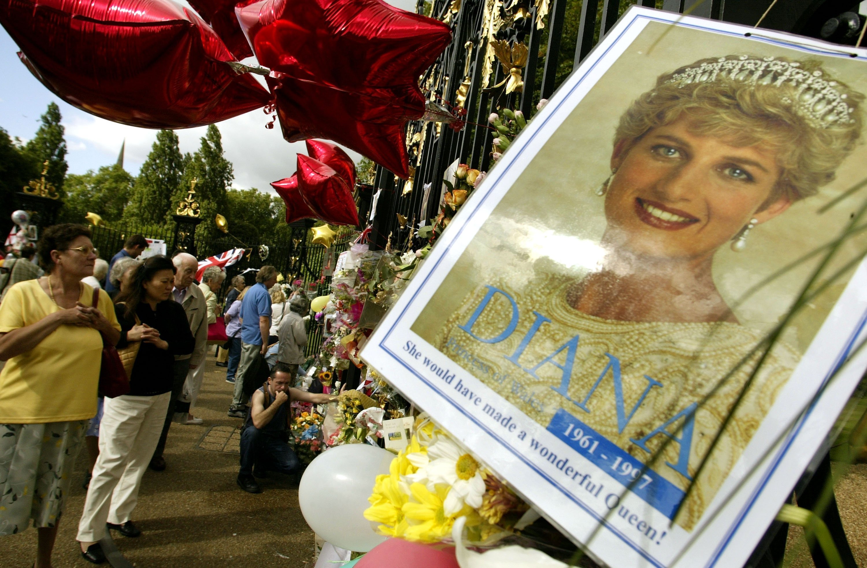 People placing flowers balloons and pictures of Princess Diana outside the gates of Kensington Palace in London, England | Photo: Getty Images