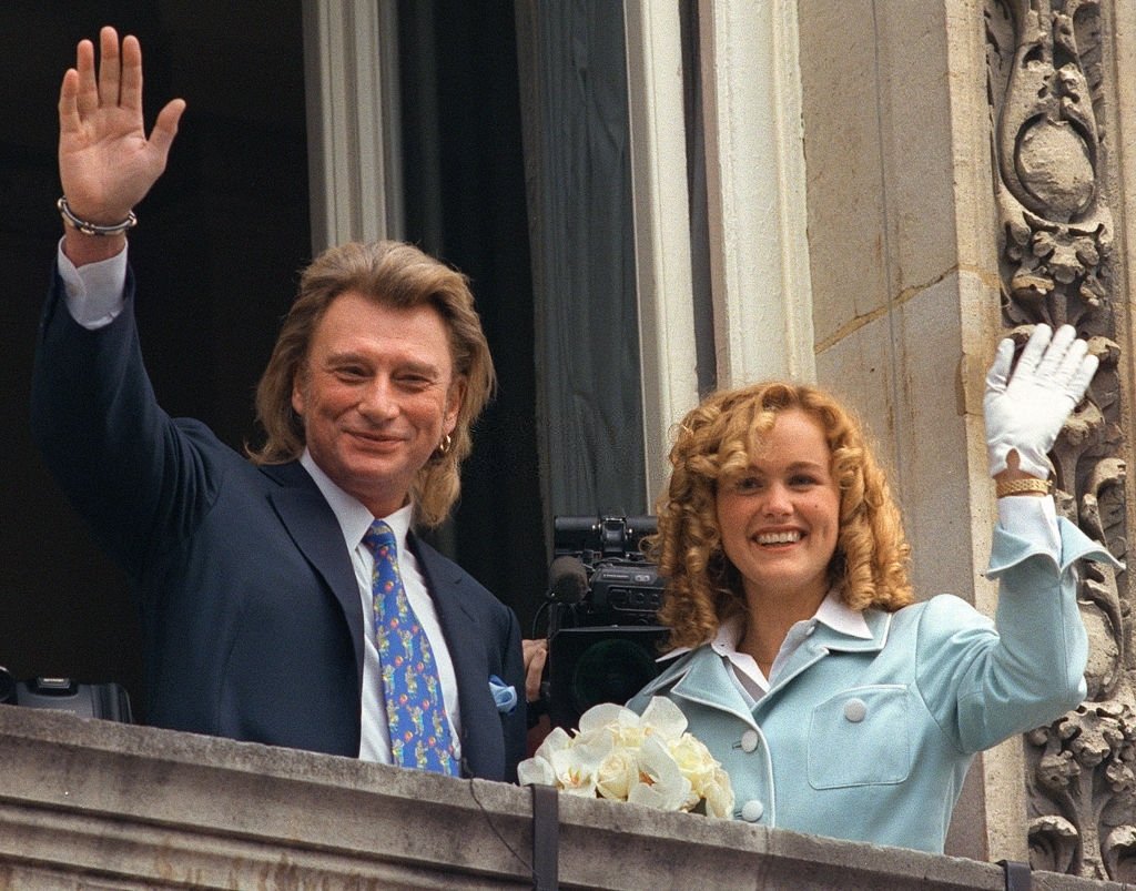 Le chanteur français, Johnny Hallyday et sa nouvelle épouse, Laeticia Boudou, saluent les nombreux fans venus assister à leur mariage célébré le 25 mars 1996 à la mairie de Neuilly-sur-Seine. | Photo : Getty Images