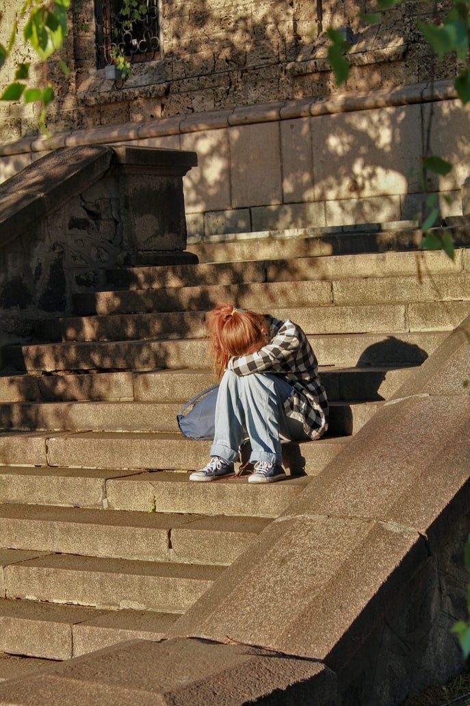Joven sentada en una escalera con su cabeza reposando sobre sus rodillas. | Foto: Unsplash