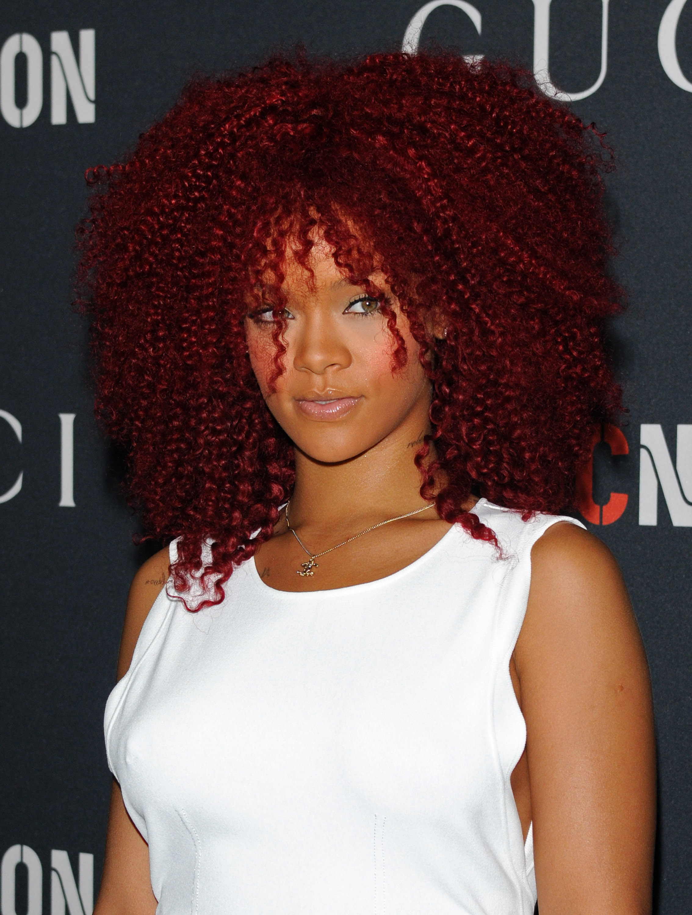 Rihanna steps into the Soho House brunch glowing with confidence, her vibrant red curled hair forming a striking halo. A crisp white dress contrasts effortlessly with her bold hair, and with a soft, knowing smile, she commands the room in a way only she can.