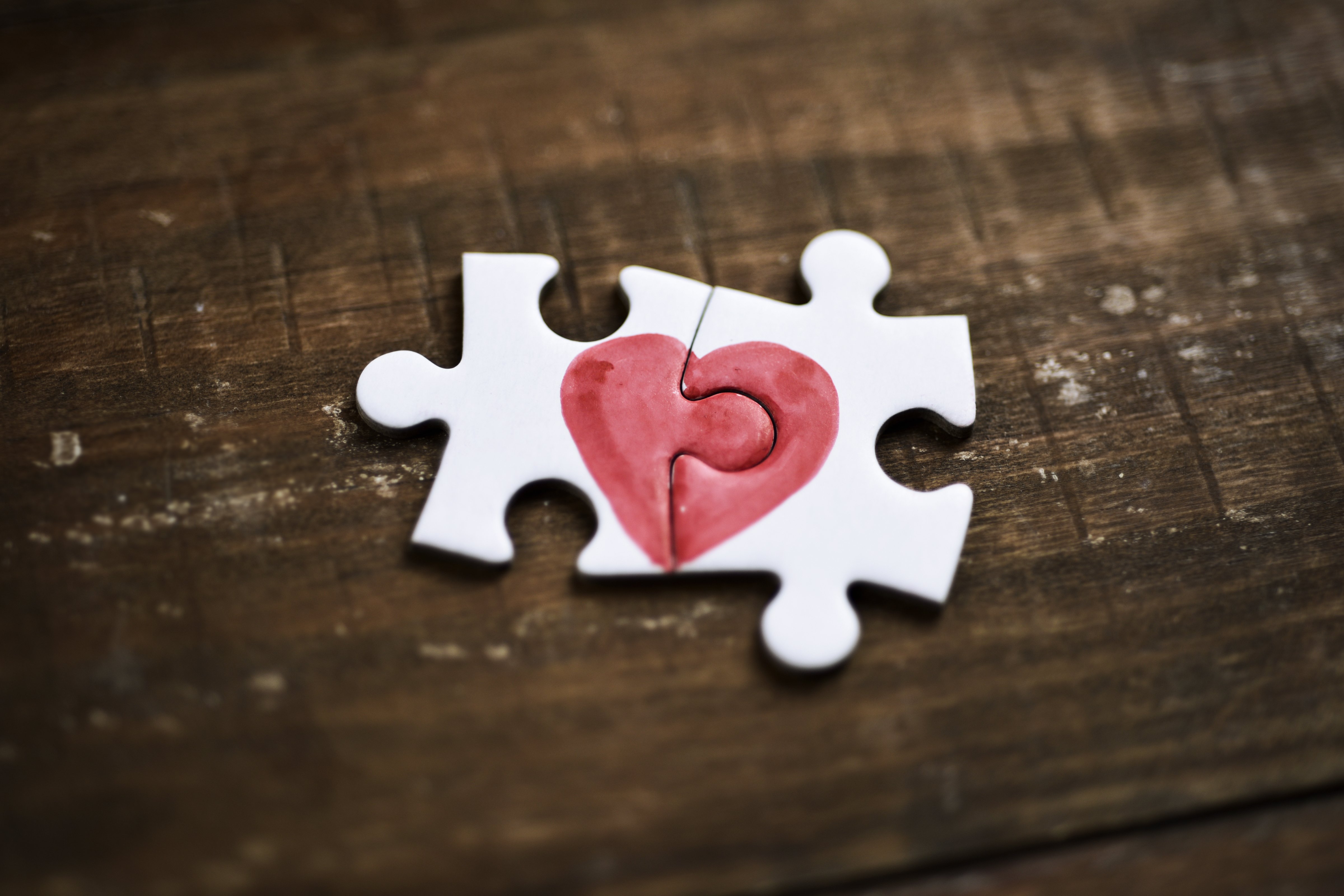 Nahaufnahme von zwei Puzzleteilen, die ein Herz auf einer rustikalen Holzoberfläche bilden. | Quelle: Shutterstock