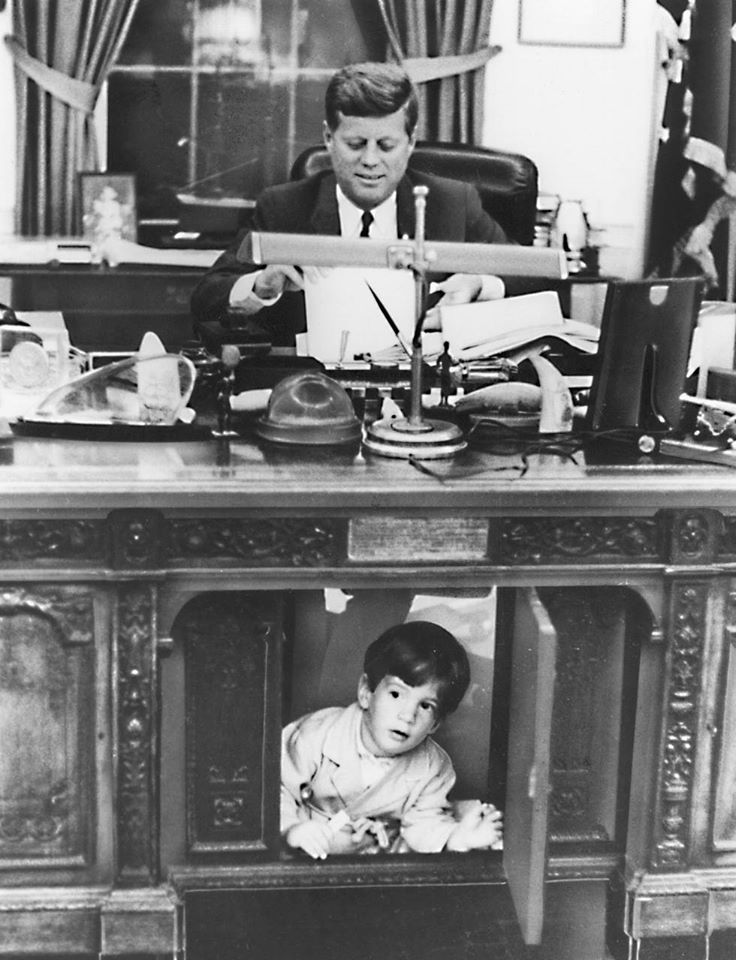 John F. Kennedy Jr. se cache sous le bureau de son père vers 1963. | Source: Wikimedia Commons