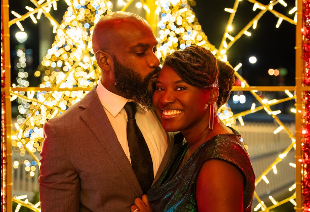 Stephen Bowen leans in to kiss Nancy Metayer Bowen on the forehead as she smiles brightly toward the camera, the couple framed by sparkling lights that give the moment a romantic, celebratory glow. | Source: Facebook/Nancy Metayer Bowen