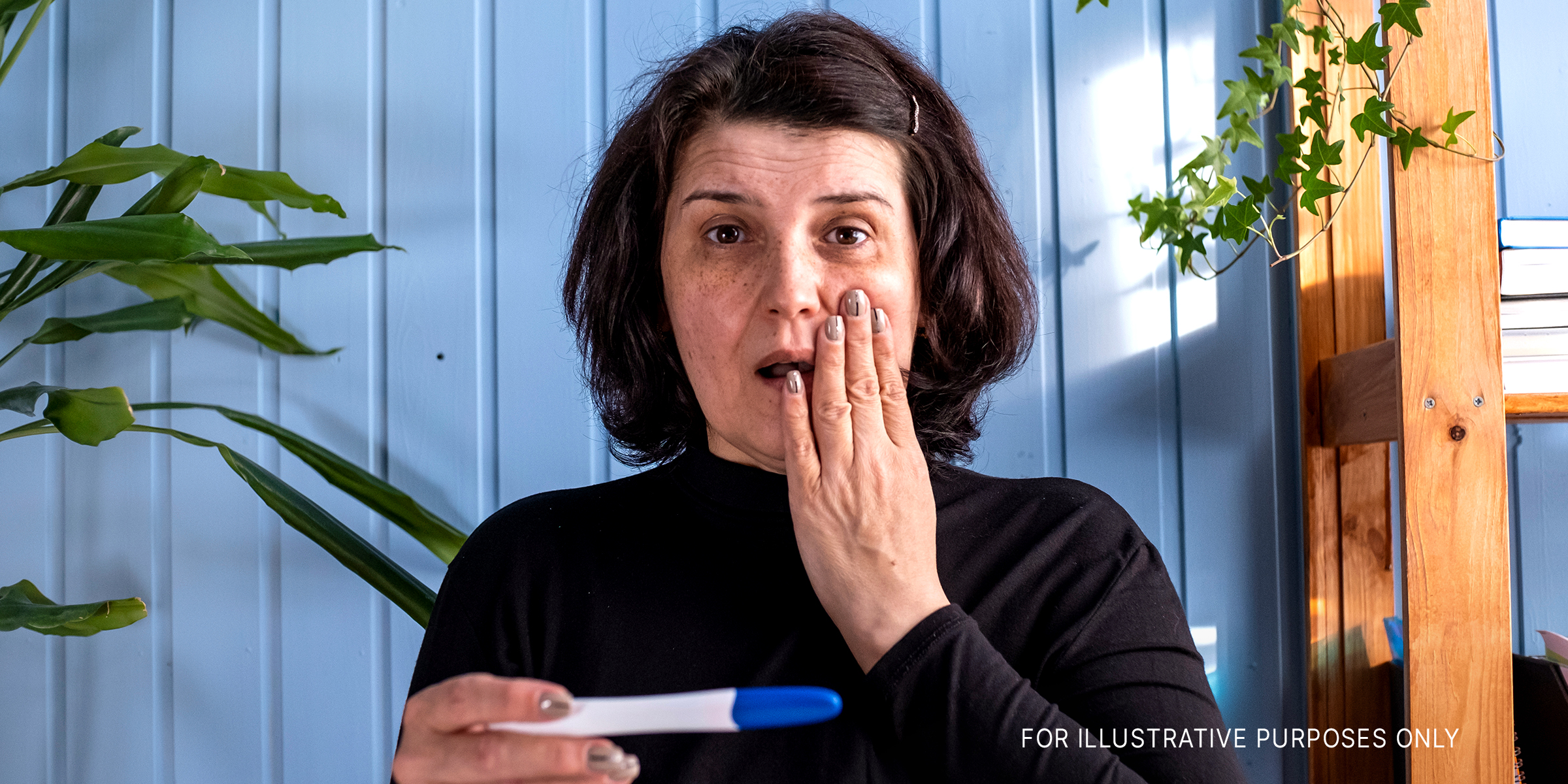 A middle-aged woman looking at a pregnancy test result showing positive | Source: Shutterstock