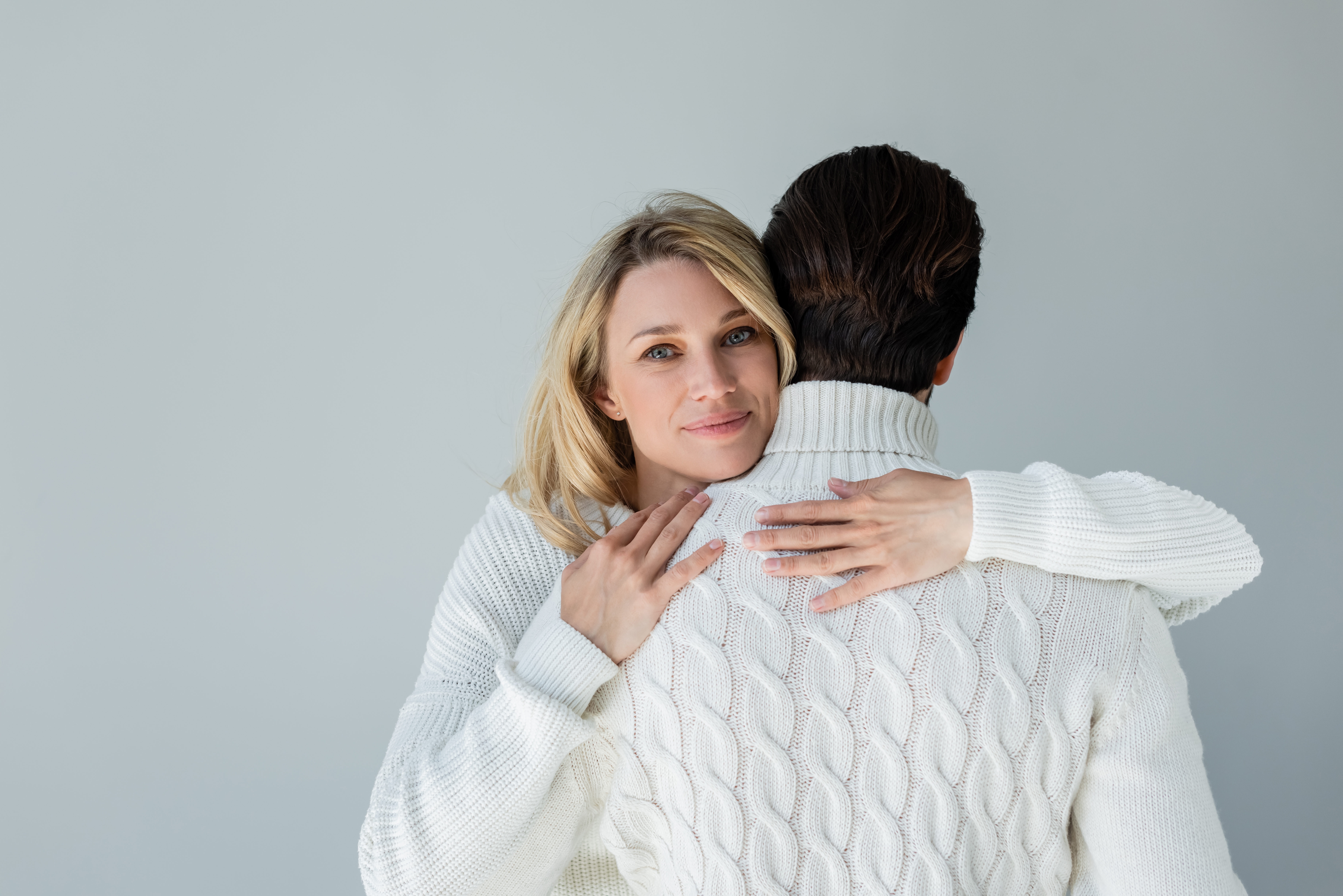 blonde wWoman in white sweater hugging back of boyfriend and smiling. | Source: Shutterstock