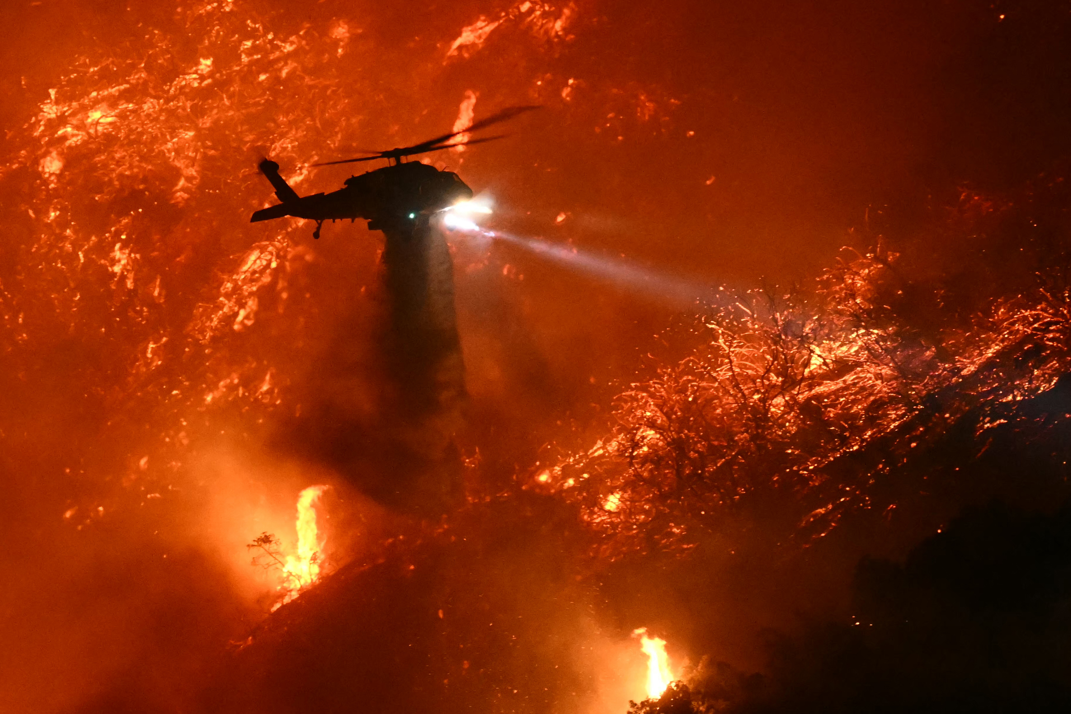 A fire fighting helicopter drops water as the Palisades fire grows near the Mandeville Canyon neighborhood and Encino, California, on January 11, 2025 | Source: Getty Images