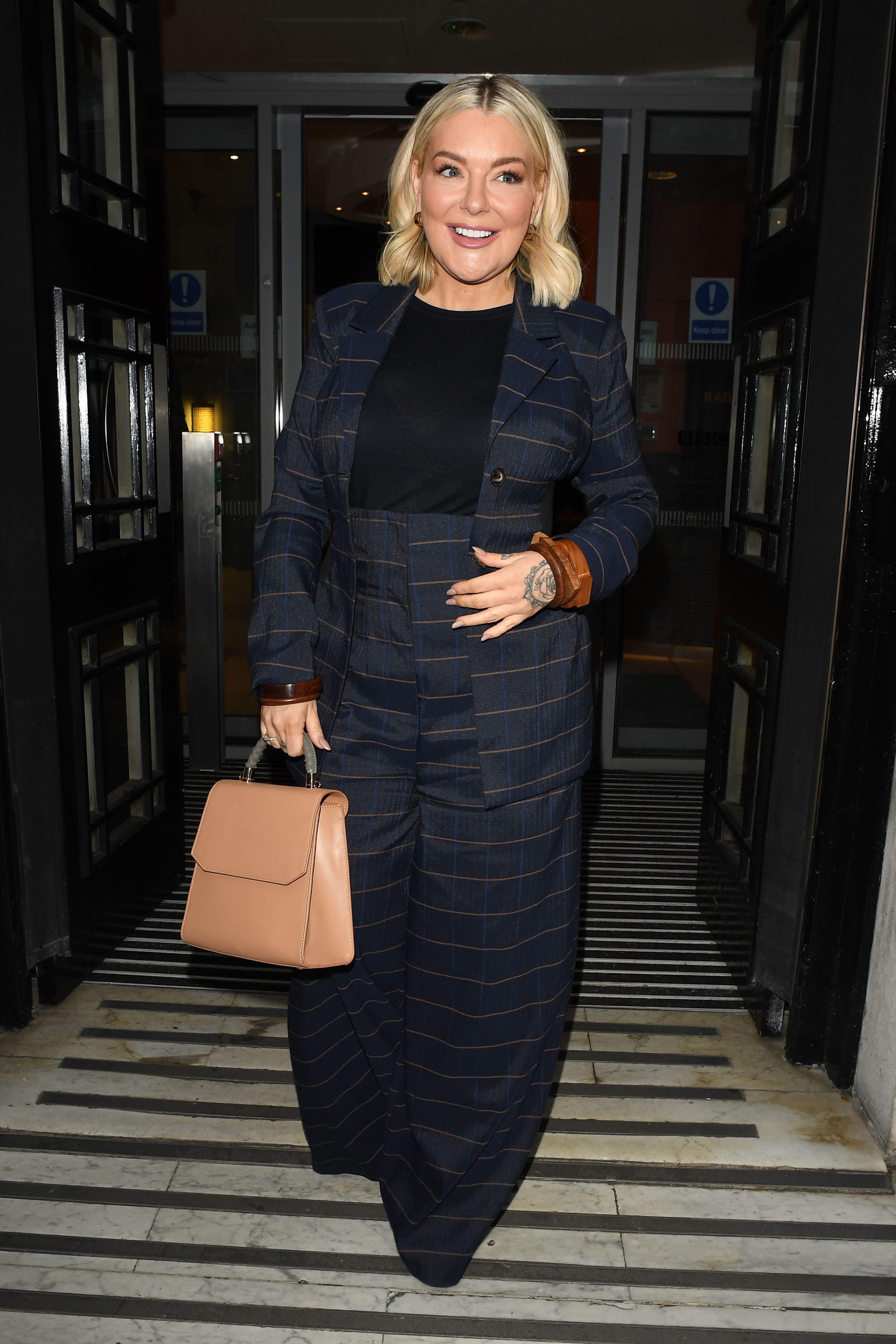 Stepping out of BBC Radio 2 in London on 9 December 2022, Smith cuts a polished figure in a wide-leg navy pinstripe suit, tan leather cuffs, and a structured camel handbag.