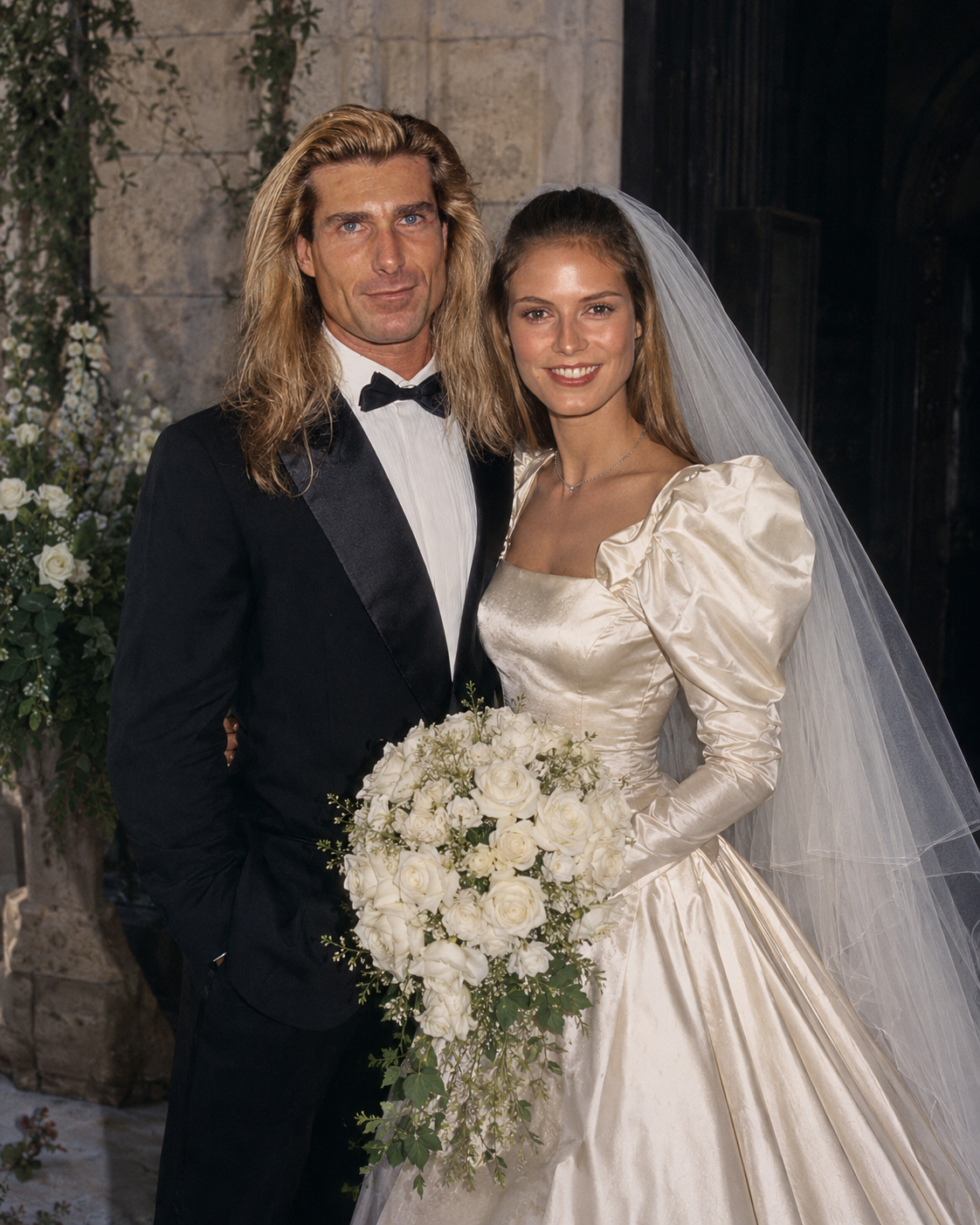 This AI creation depicts Fabio in a classic black tuxedo standing alongside Heidi Klum in a satin wedding gown with puff sleeves and a flowing veil, capturing vintage bridal elegance. | Source: ChatGPT