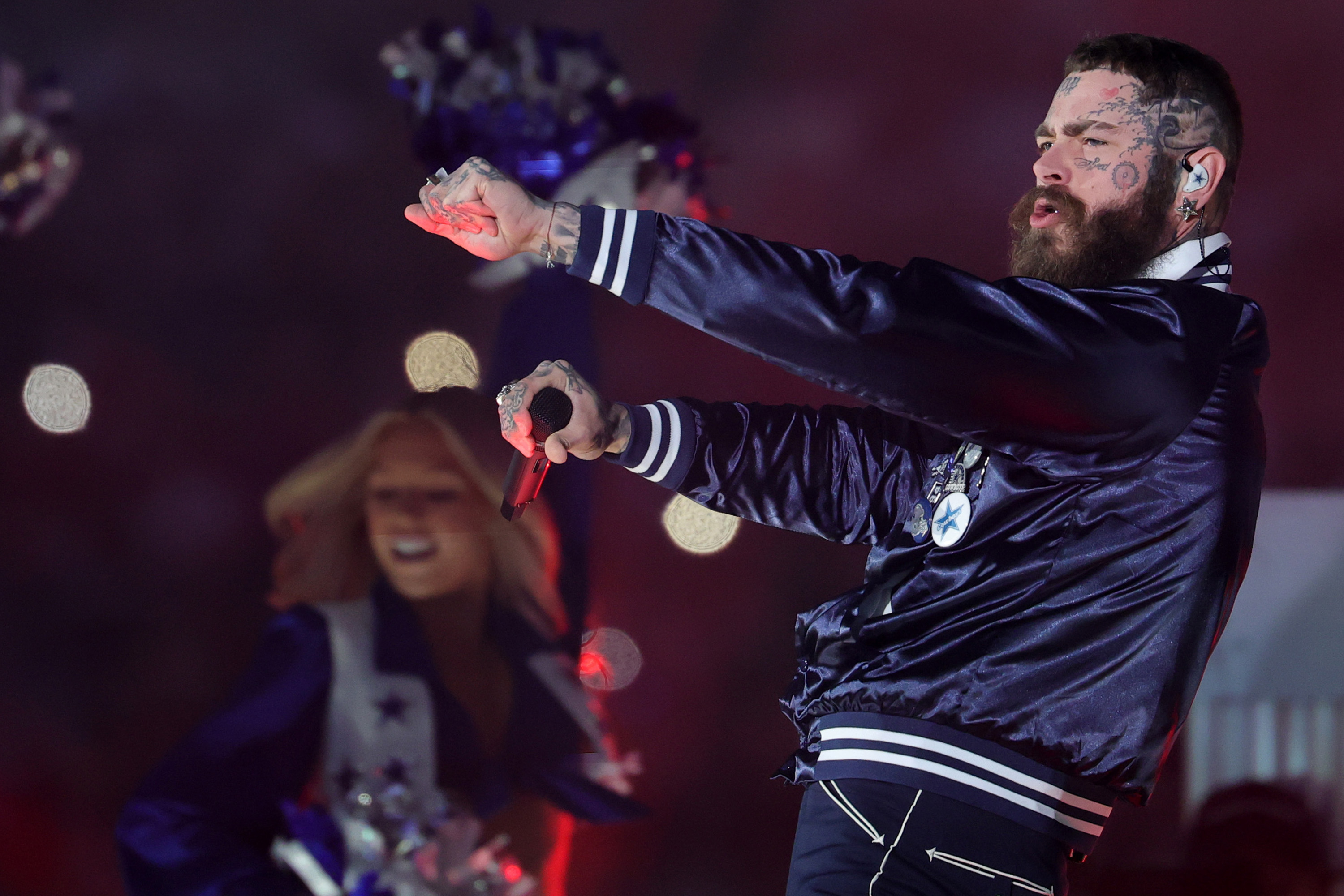 Post Malone extends his left arm and raises his right fist near his face while singing during his halftime performance on November 27, 2025 | Source: Getty Images