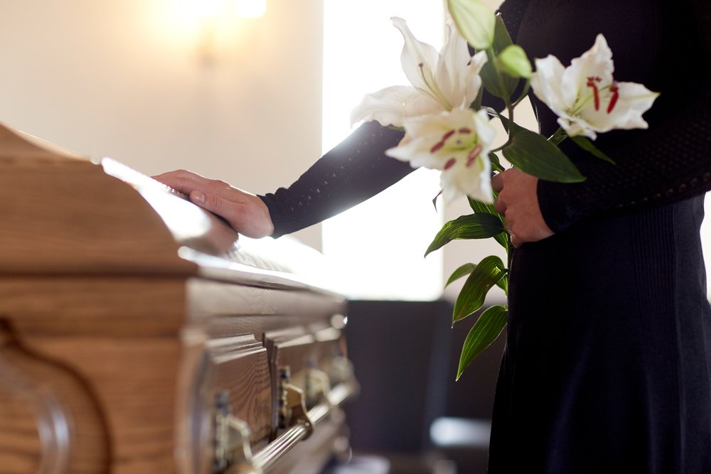 A woman with white lily flowers holding a coffin at a funeral. | Photo: Shutterstock
