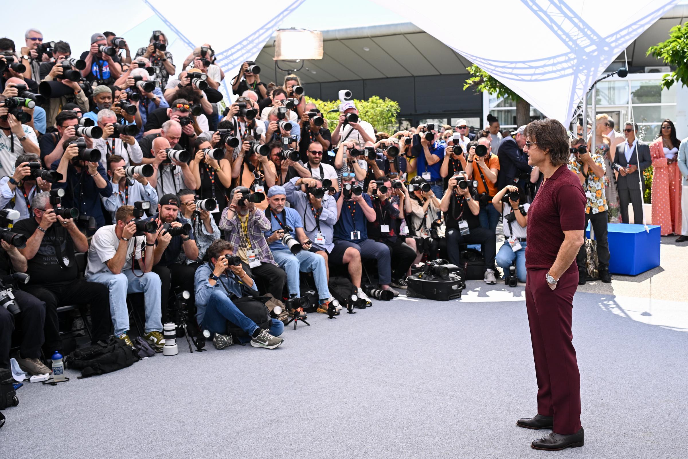 Tom Cruise stands poised with his hands in his pockets as a sea of photographers captures the moment at the "Mission: Impossible – The Final Reckoning" photocall in Cannes. His calm presence contrasts the flurry of camera shutters around him.