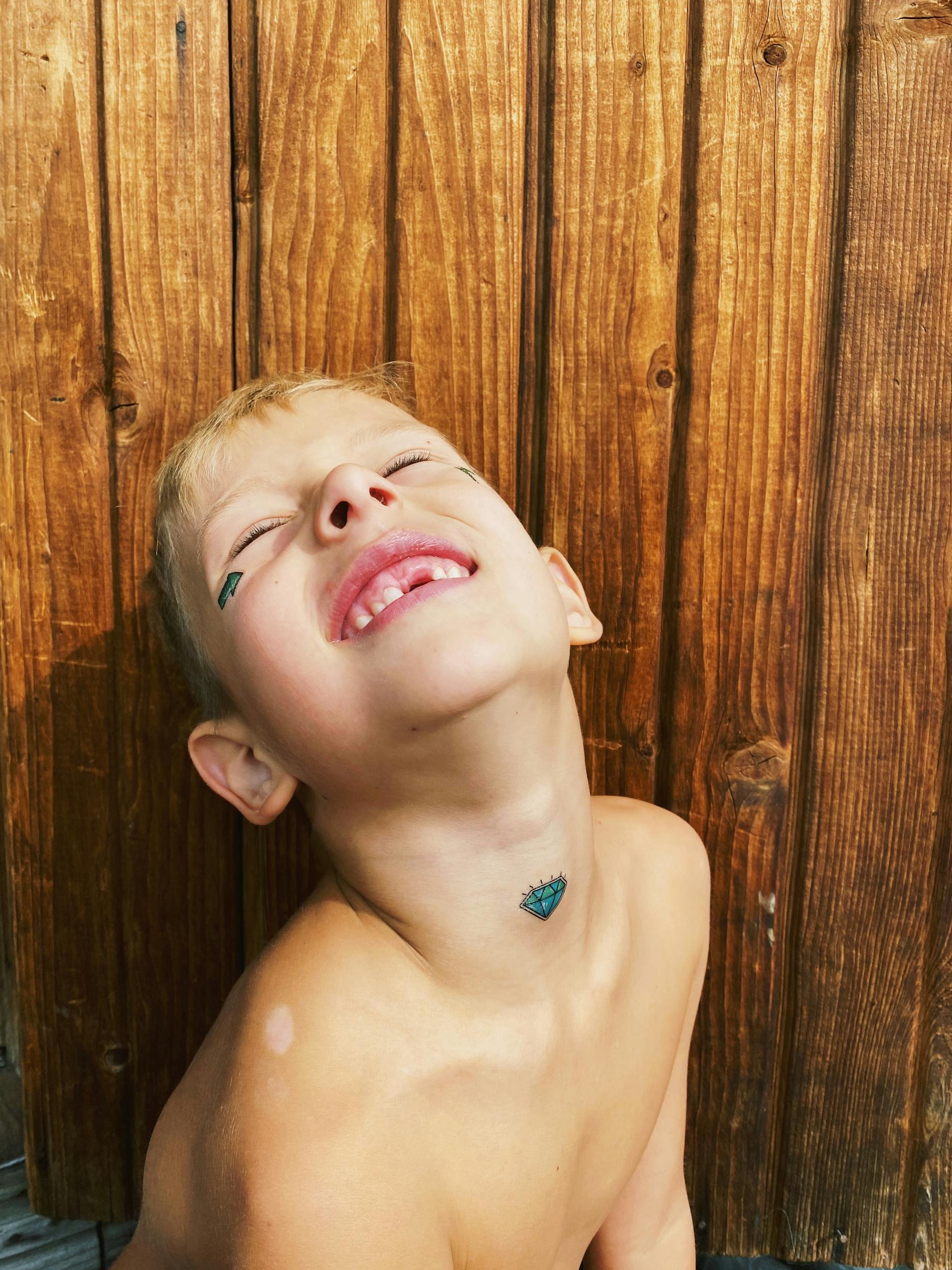 A topless boy with a missing front tooth leaning against a wall | Source: Pexels