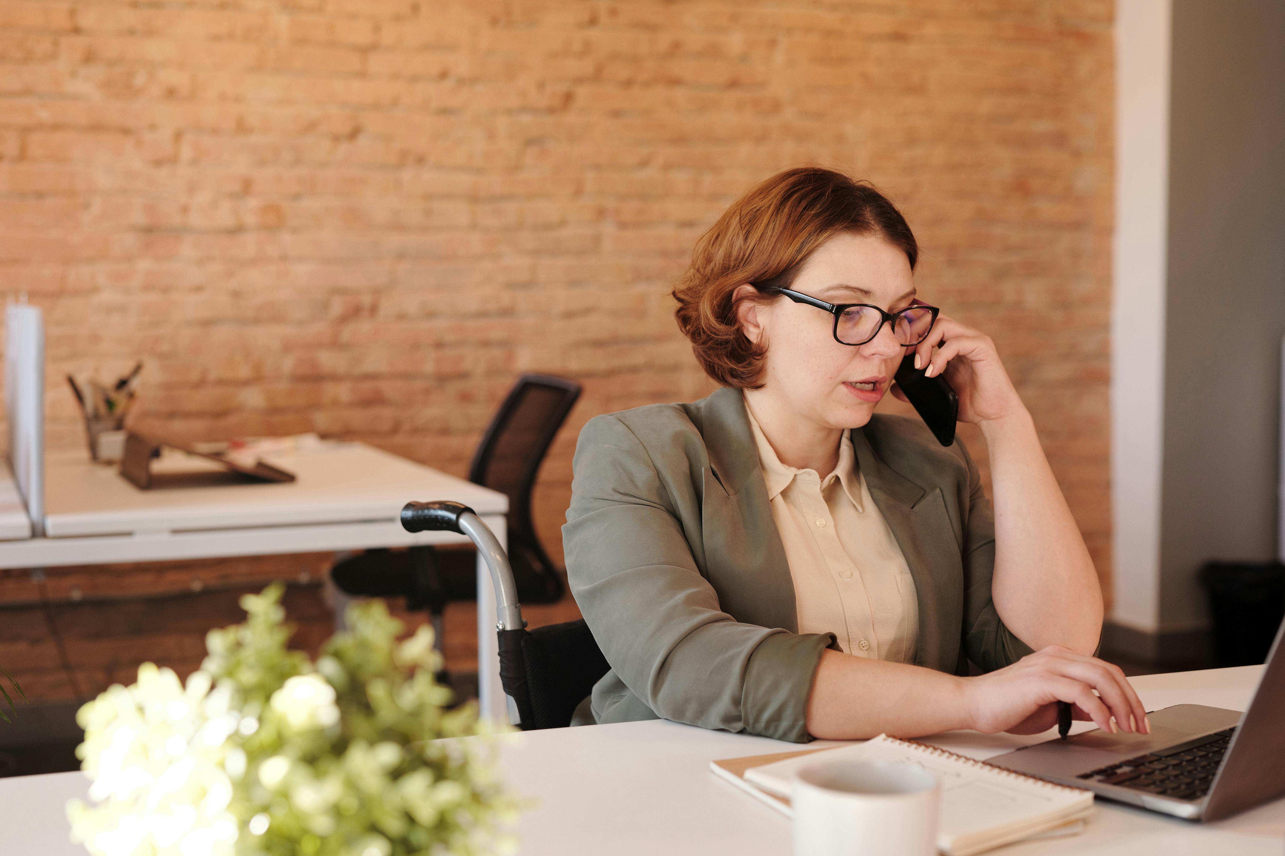 Una mujer hablando por teléfono mientras trabaja en una computadora portátil | Fuente: Pexels