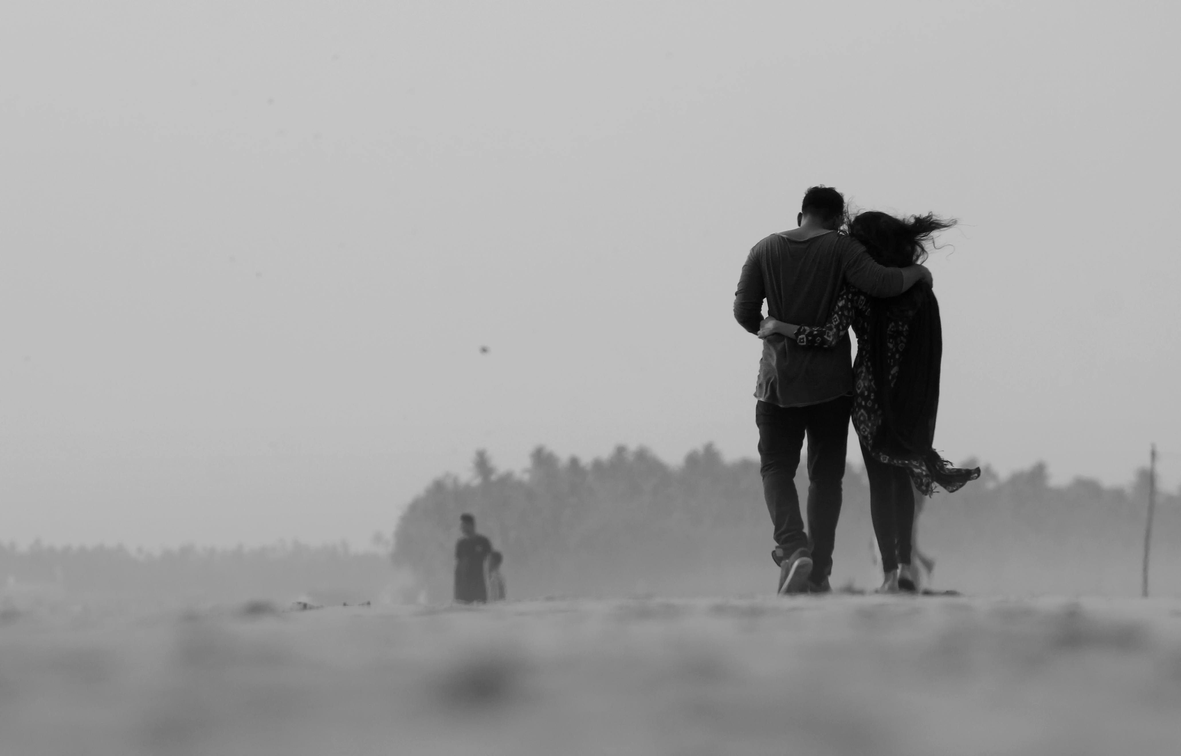 A black and white photo of a couple leaning on one another and walking away from the camera | Source: Pexels