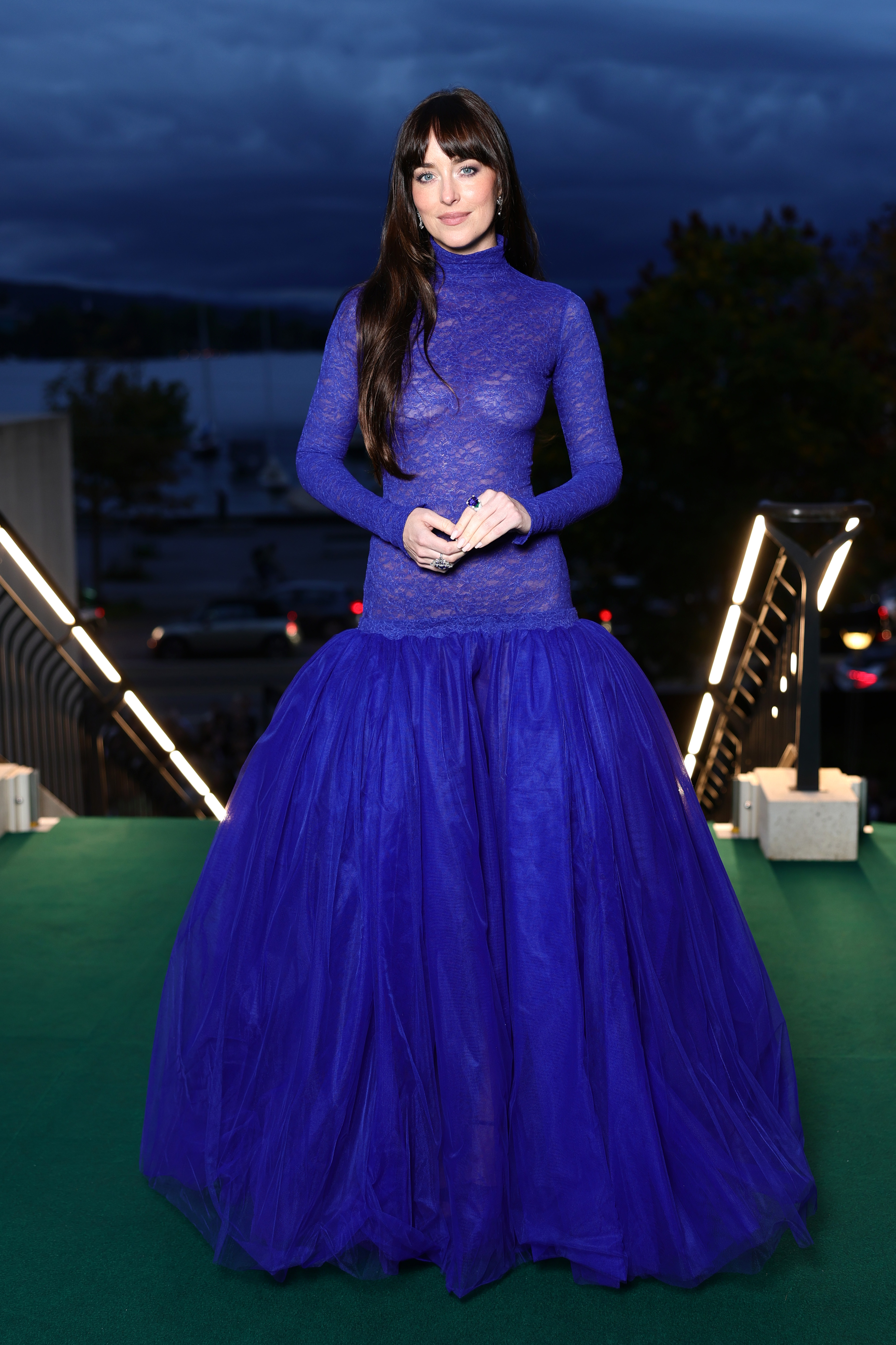 Dakota Johnson makes a dramatic entrance on the green carpet during the 21st Zurich Film Festival, wearing a bold, body-skimming cobalt lace gown with a voluminous tulle skirt that adds regal flair. With cascading brunette waves and sparkling statement rings, she commands attention.