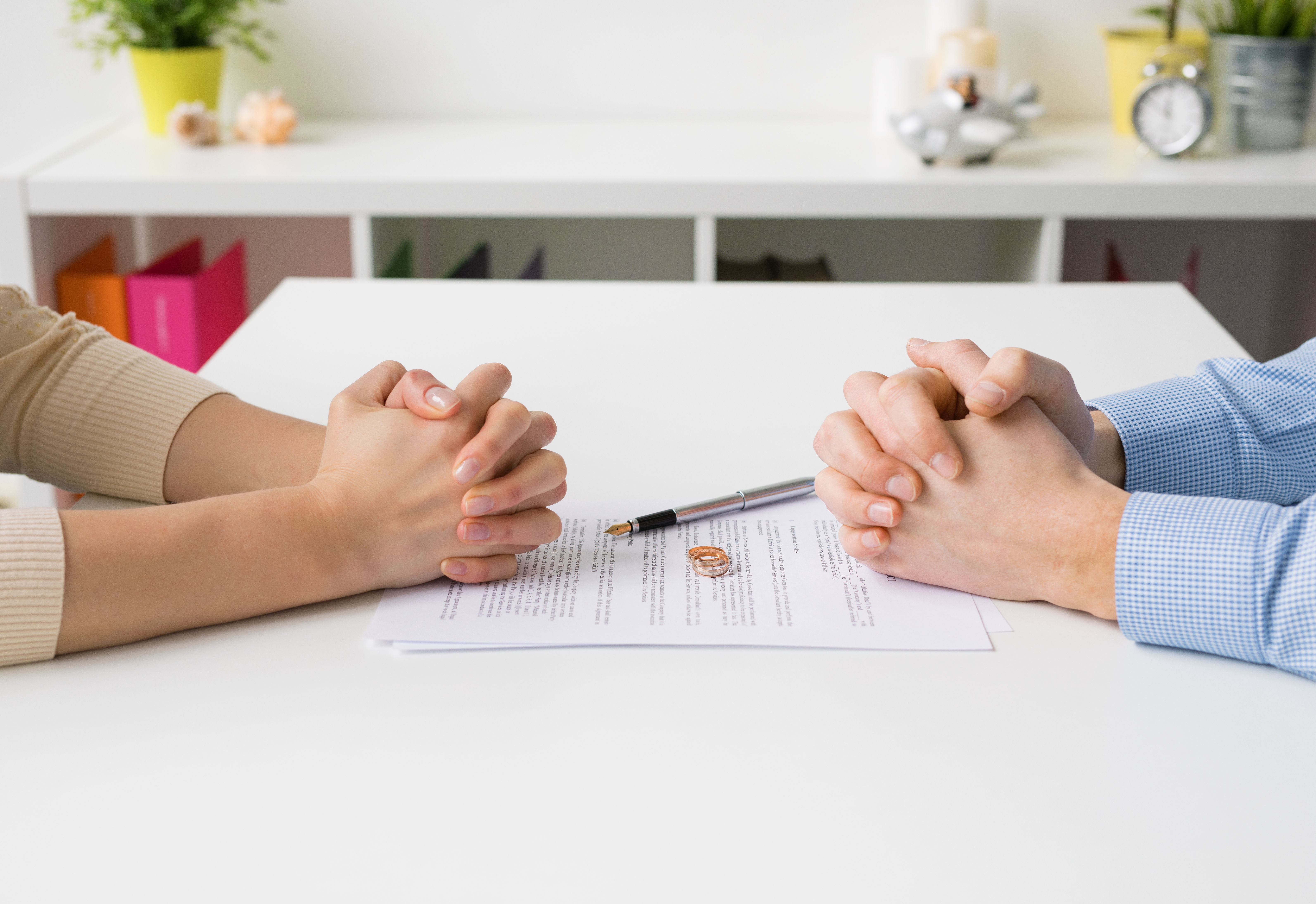 A man and woman's hands on a table with their wedding rings and divorce papers in front of them | Source: Shutterstock