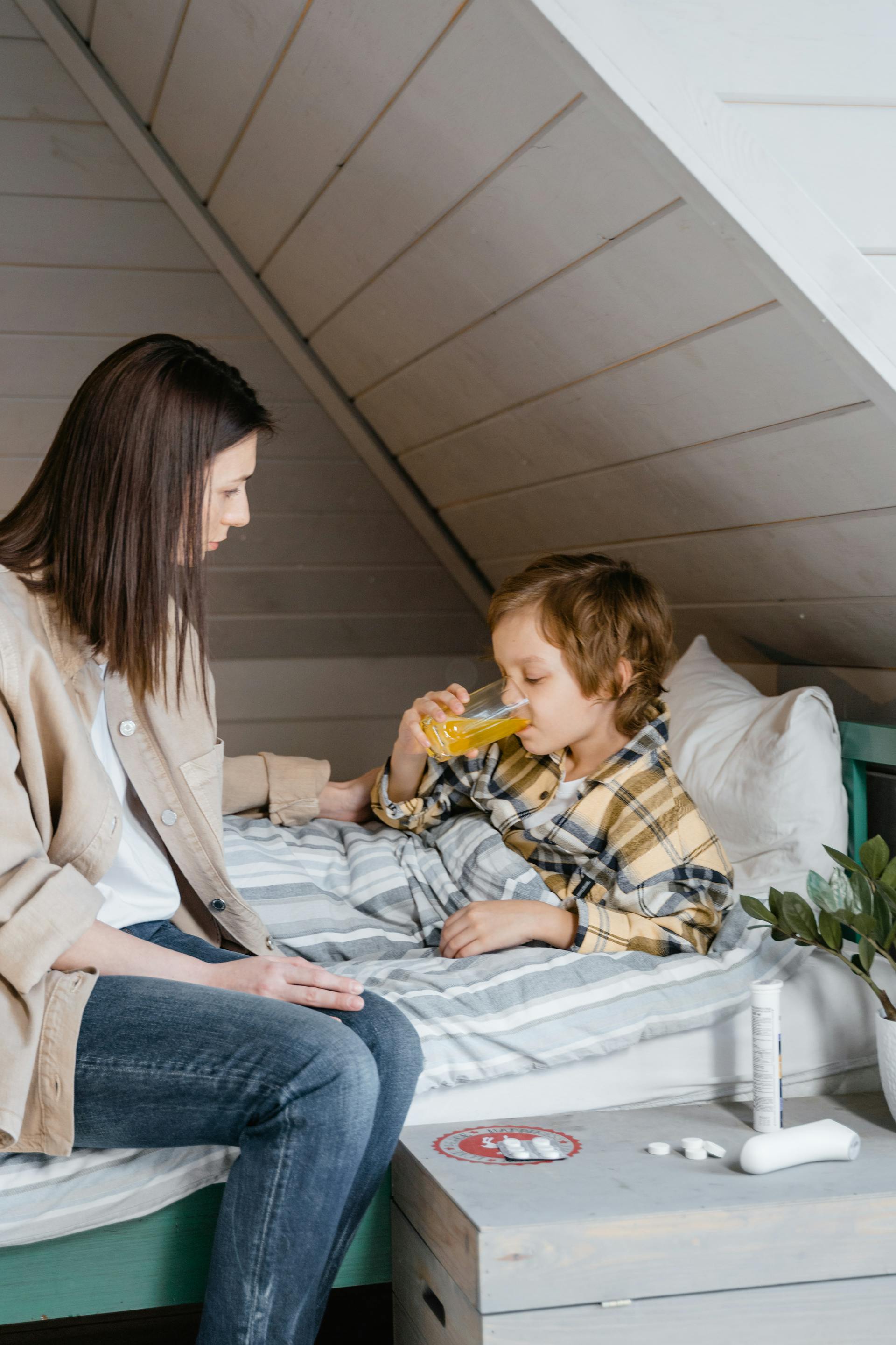 A woman looks at her young son drinking juice in bed | Source: Pexels