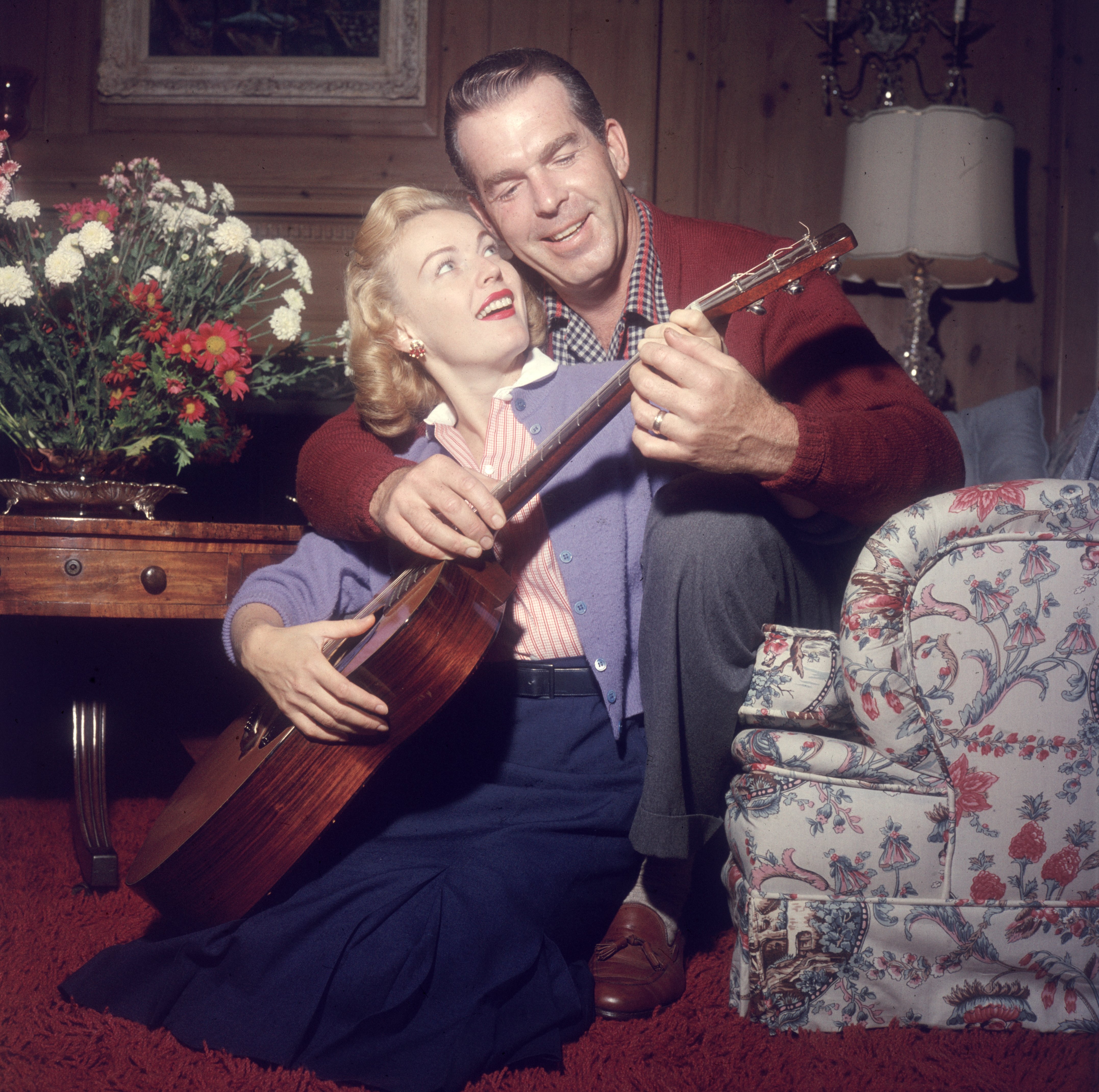 Fred MacMurray shows his wife, actor June Haver, how to play the guitar while sitting behind her on the living room floor. | Source: Getty Images