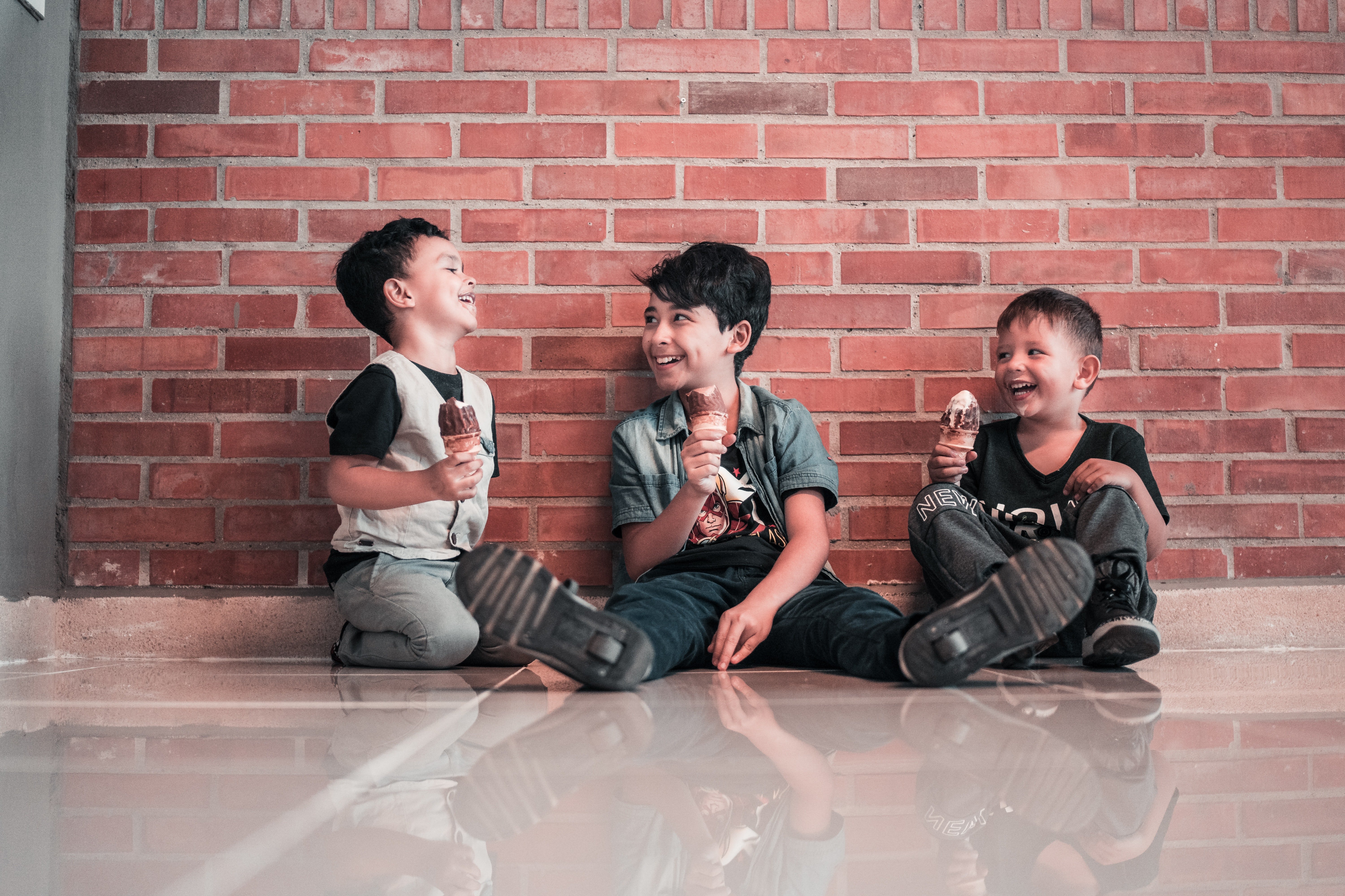 Tres niños sonrientes sentados en el suelo. | Foto: Pexels