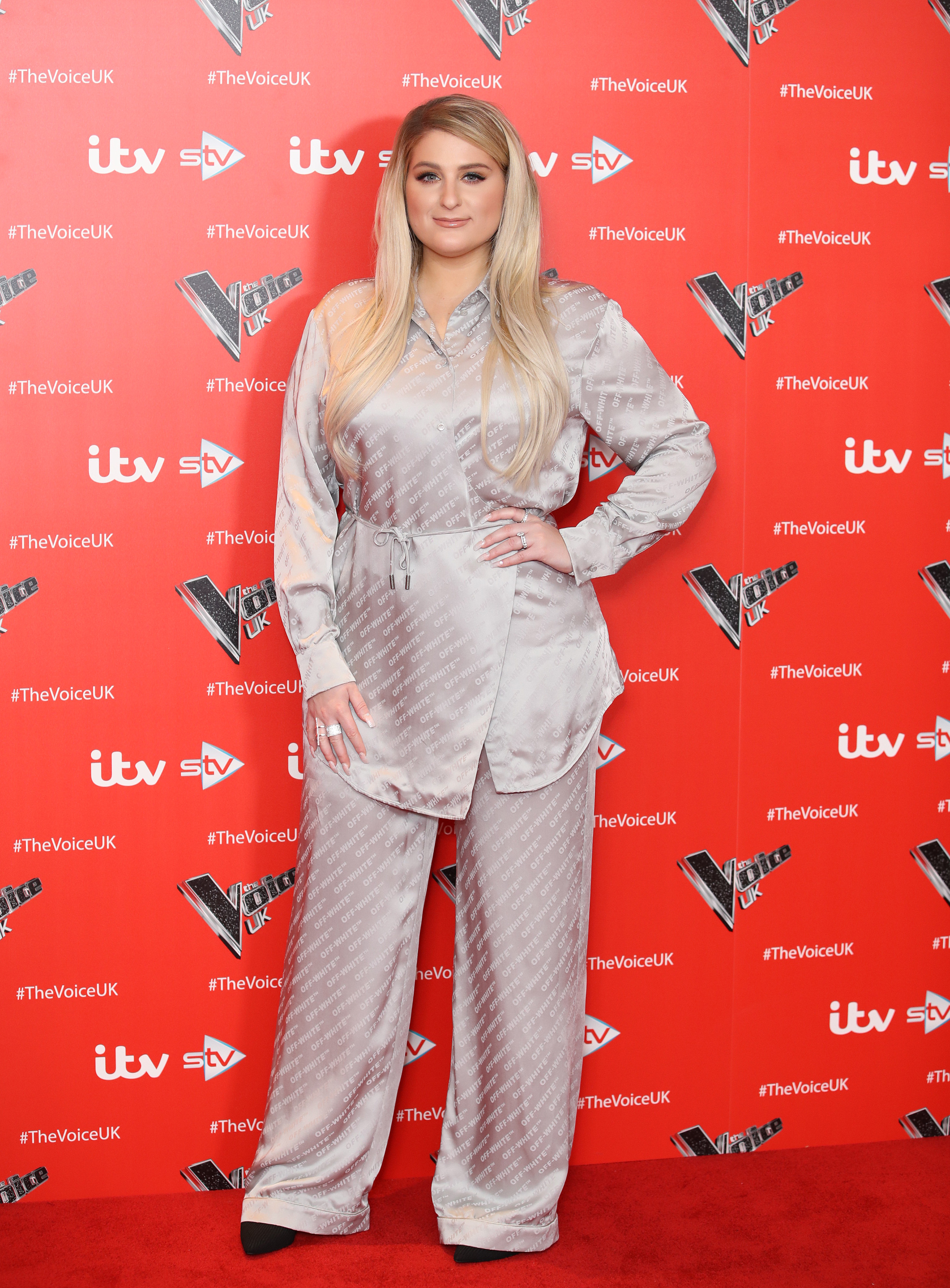 Meghan Trainor attends The Voice UK in 2019 wearing a shiny silver pajama-inspired set, cinched at the waist, with sleek hair and soft glam, offering a cozy yet stylish red carpet moment.