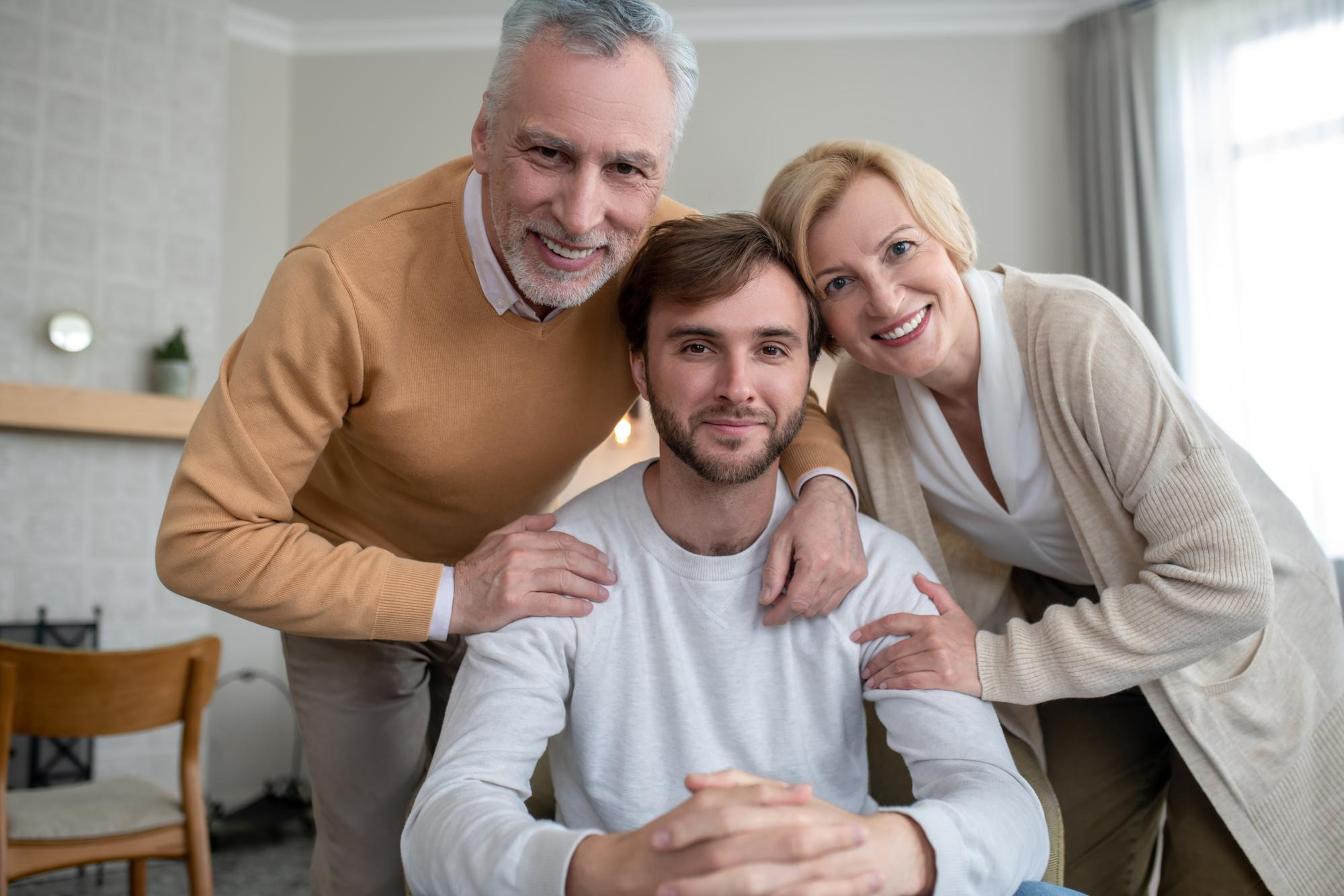 A young man sandwiched in an embrace by his proud parents | Source: Freepik