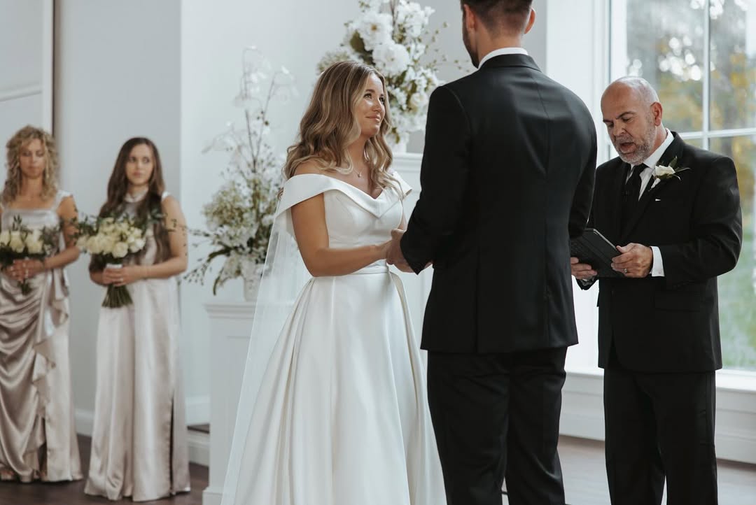 With bridesmaids standing nearby, Jana Duggar gazes at Stephen Wissmann as they exchange vows, framed by white florals and natural light streaming in. | Source: Instagram/janamduggar