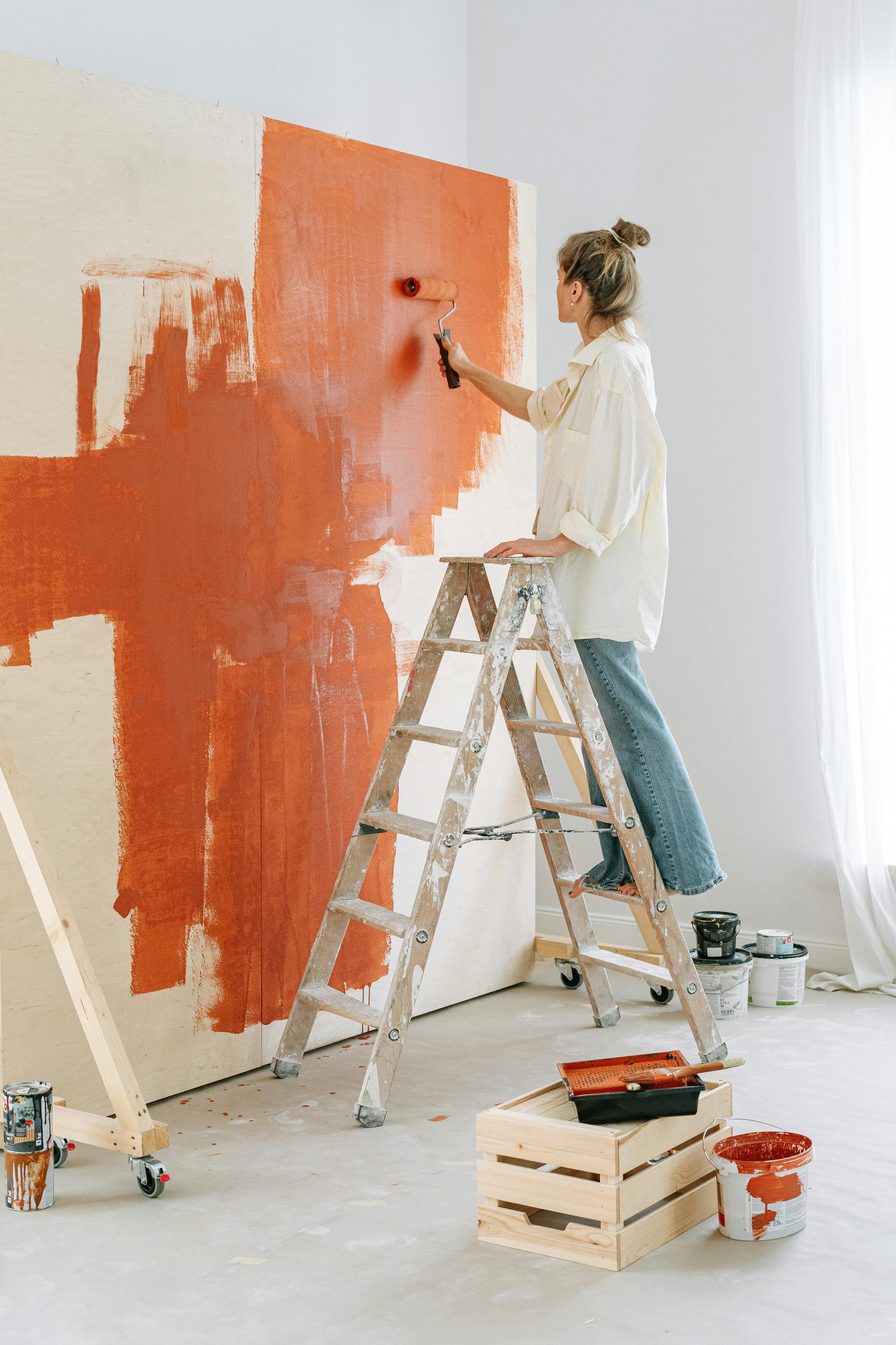 Woman standing on a stepladder painting a wall with a roller | Source: Pexels