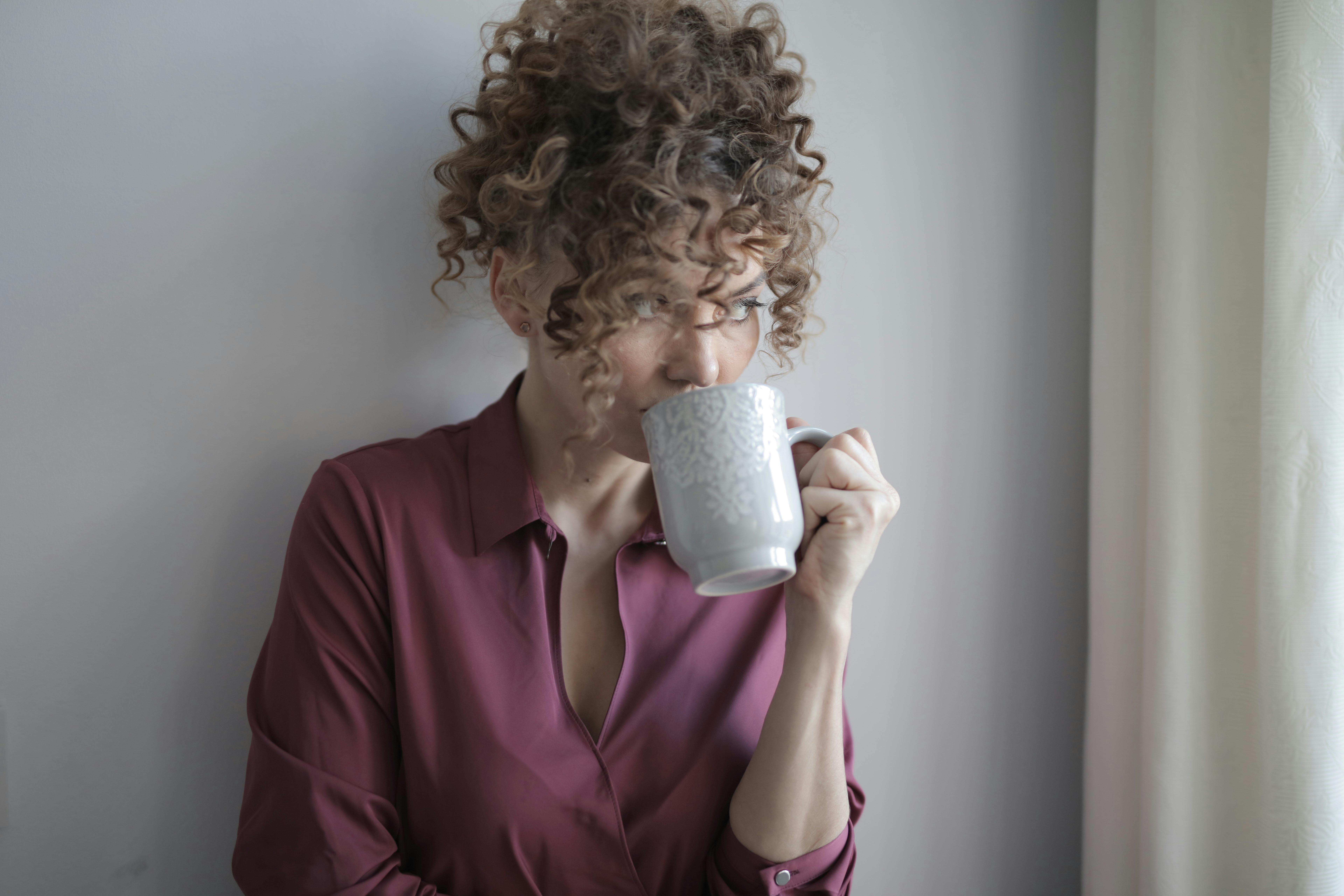 A woman sipping from a cup, looking thoughtfully out of a window | Source: Pexels