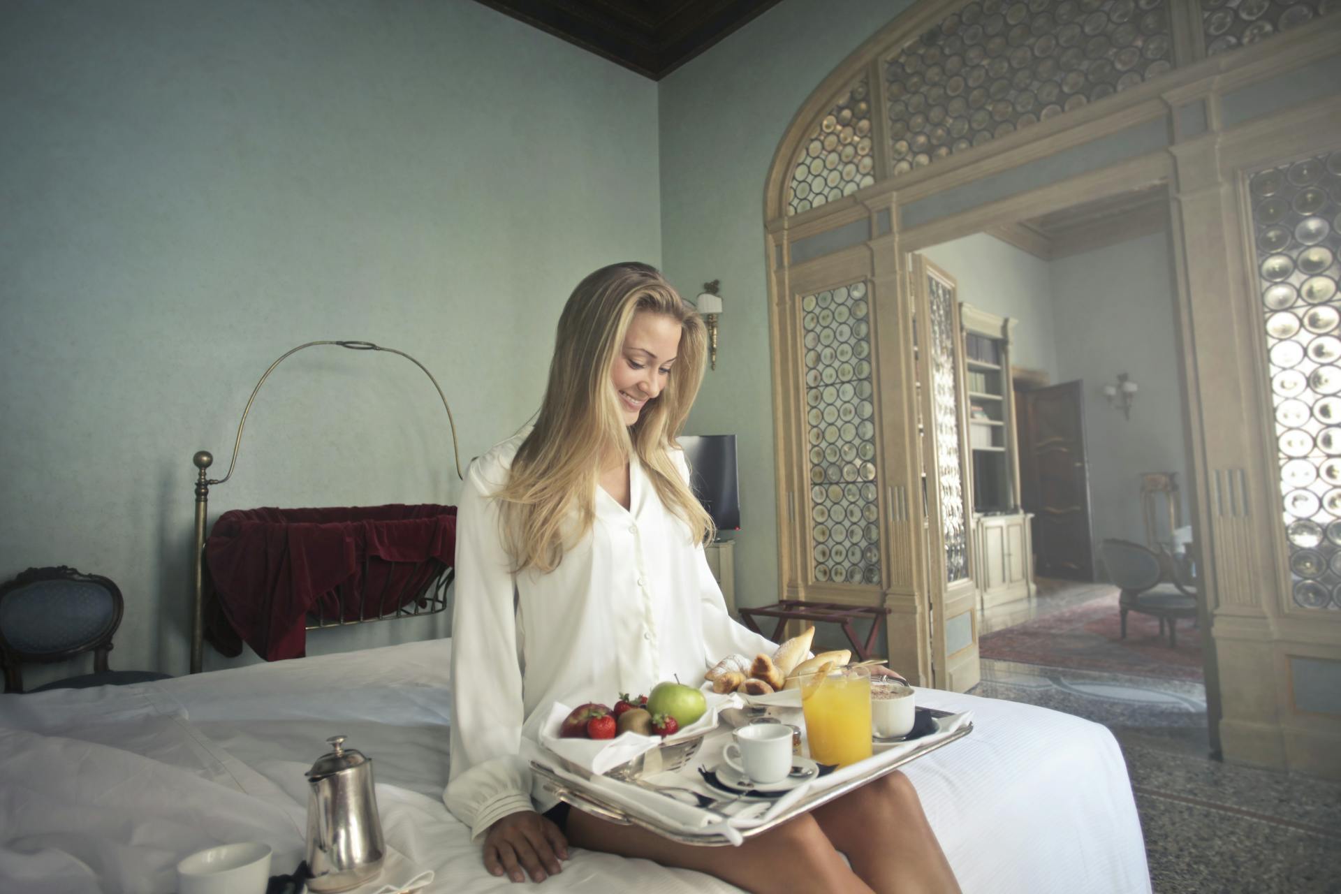 A cheerful woman with breakfast on a tray in a hotel bedroom | Source: Pexels