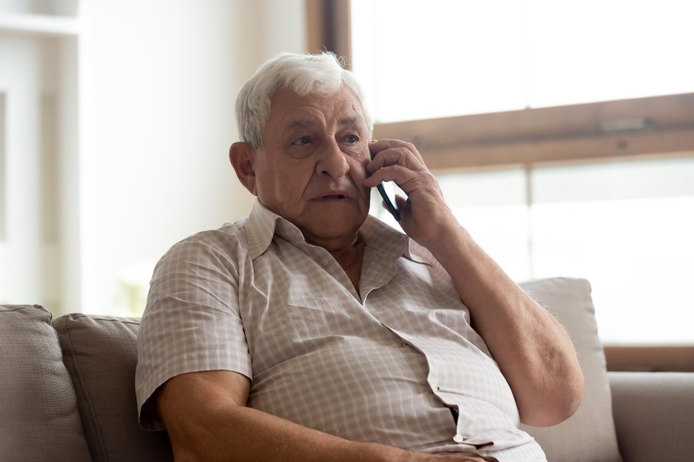 Elderly man in casual clothes seated on couch in living room making a phone call. | Photo: Shuterstock.