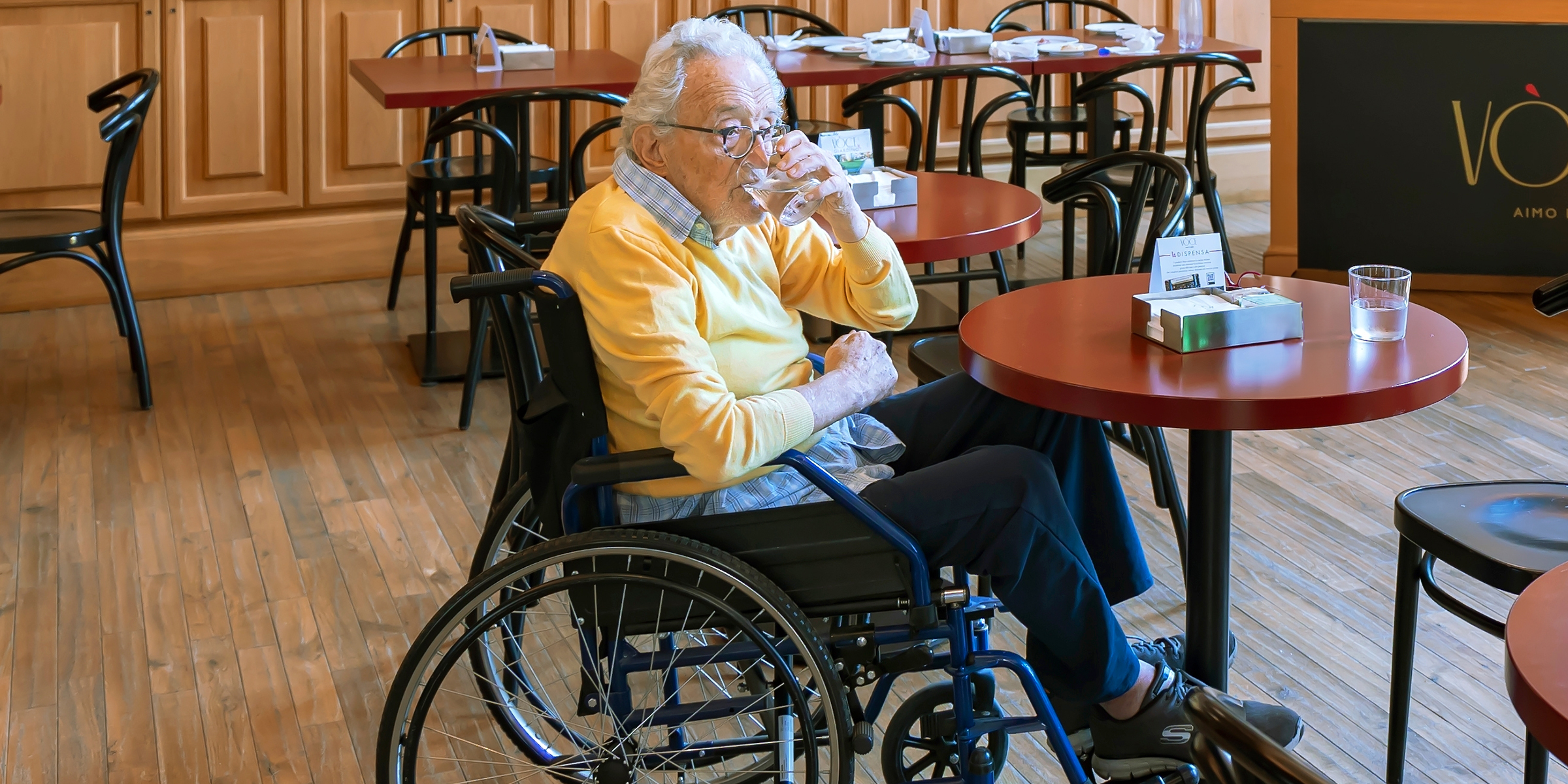 An elderly man in a wheelchair drinking water in a restaurant | Source: Shutterstock