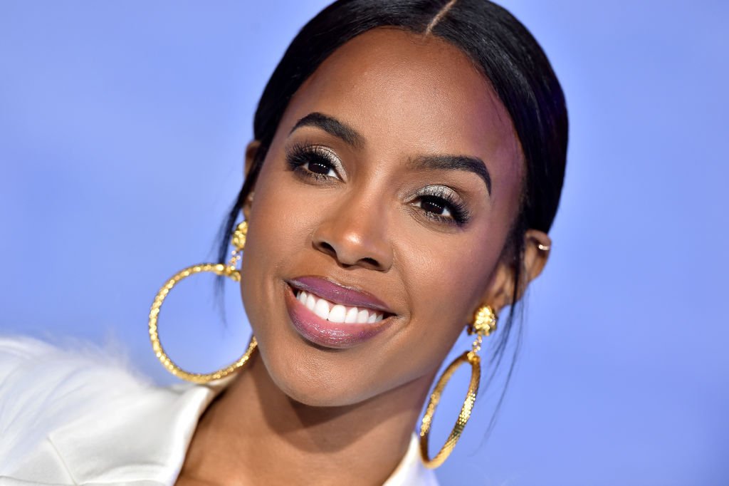 Kelly Rowland Flaunts Ample Cleavage & Curves in Purple Tassel Jumpsuit