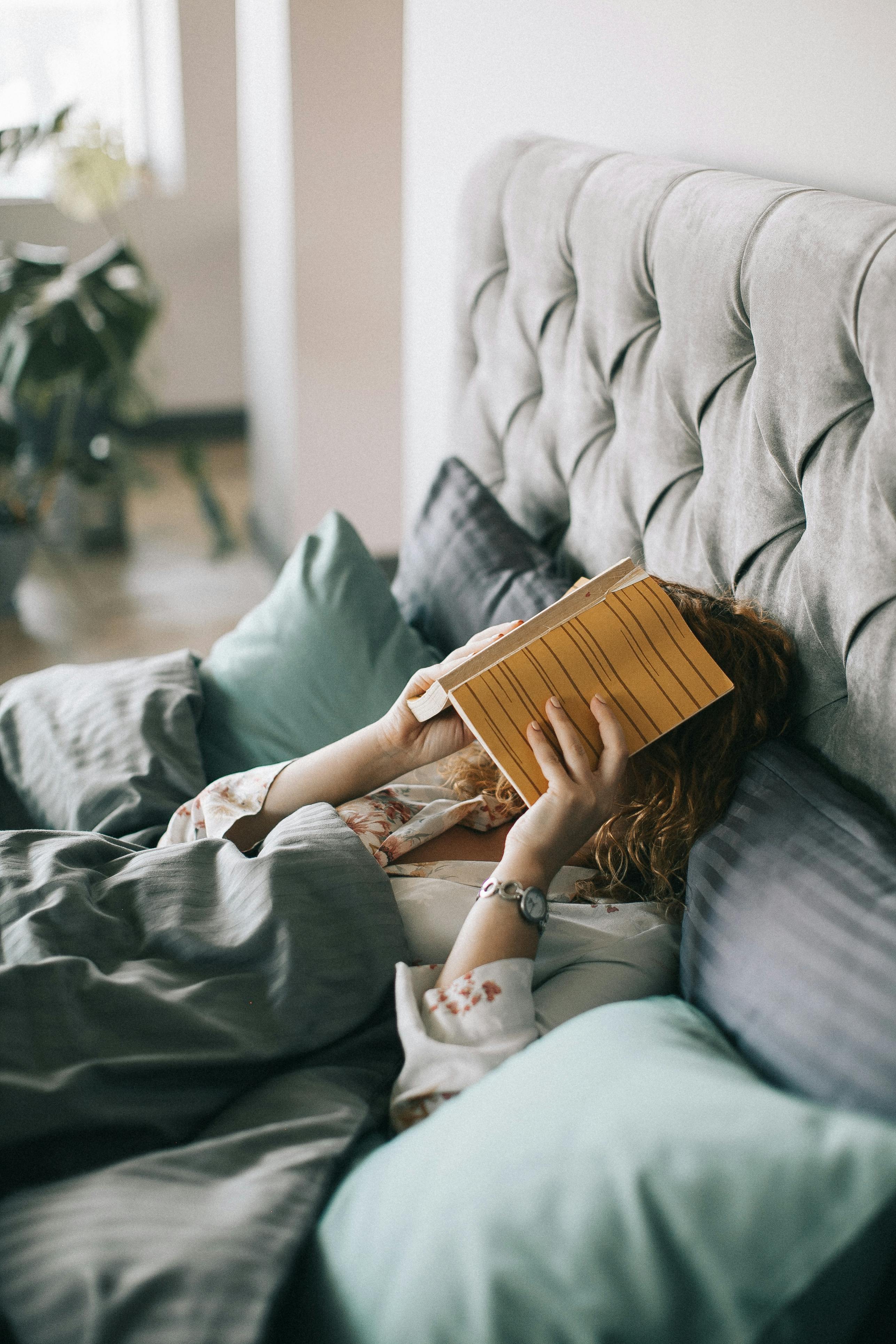 A woman lying in bed with a book covering her face | Source: Pexels