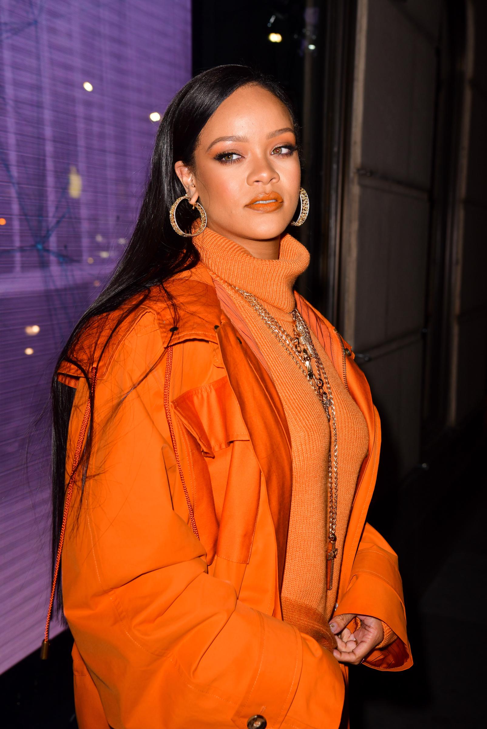 Rihanna steps into Bergdorf Goodman draped in sunset-orange layers, glowing under the city lights. Her sleek  hair and gold accessories echo the warmth of her palette, turning a simple arrival into a runway moment.