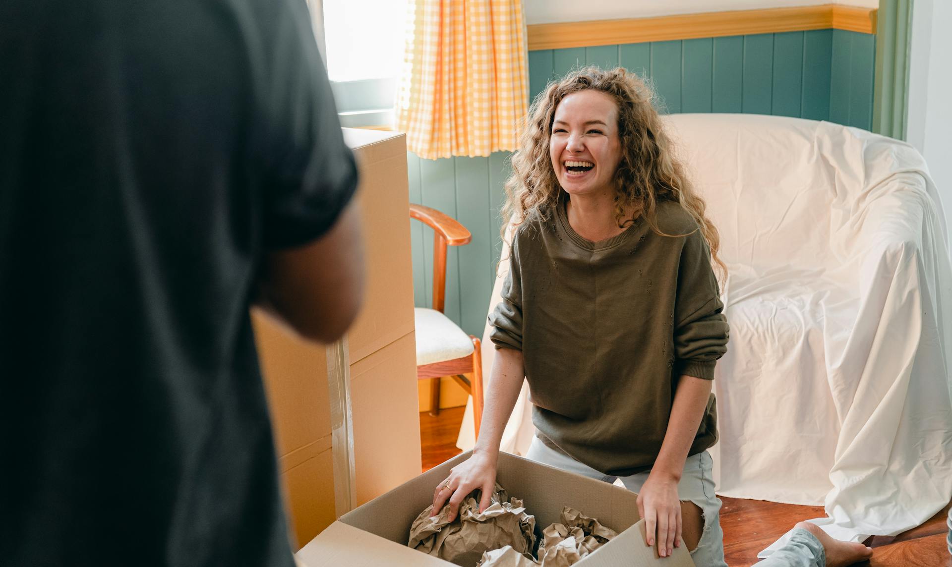 A woman sitting near a box of clothes laughs while looking at her husband | Source: Pexels