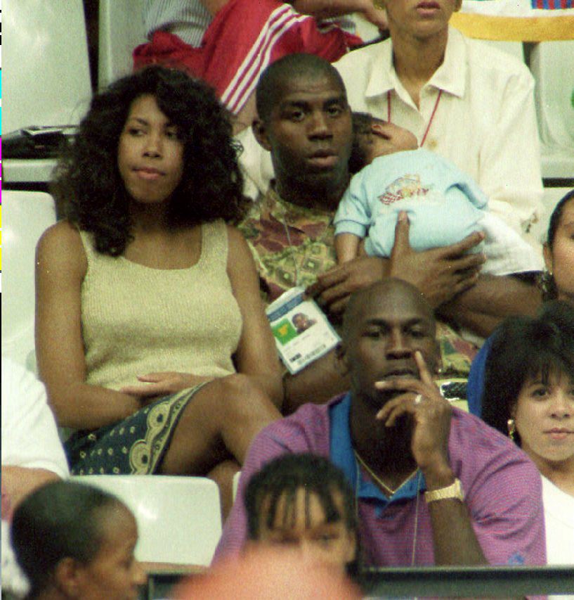 Earvin Magic Johnson holds his son, Earvin Johnson III, while watching the U.S. women's basketball team play Spain on August 3, 1992, in Barcelona, Spain, next to his wife Cookie and above Michael Jordan.